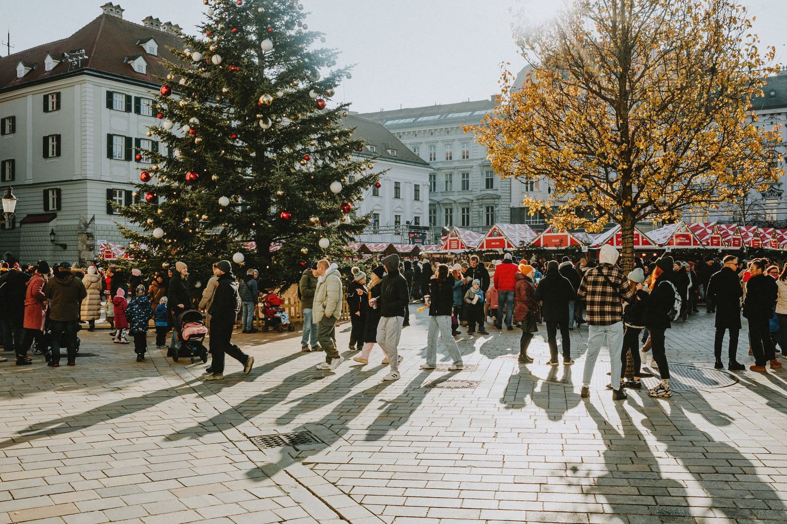 Drukke markt in een oude binnenstad met mensen tussen tentjes en feestvlaggen.