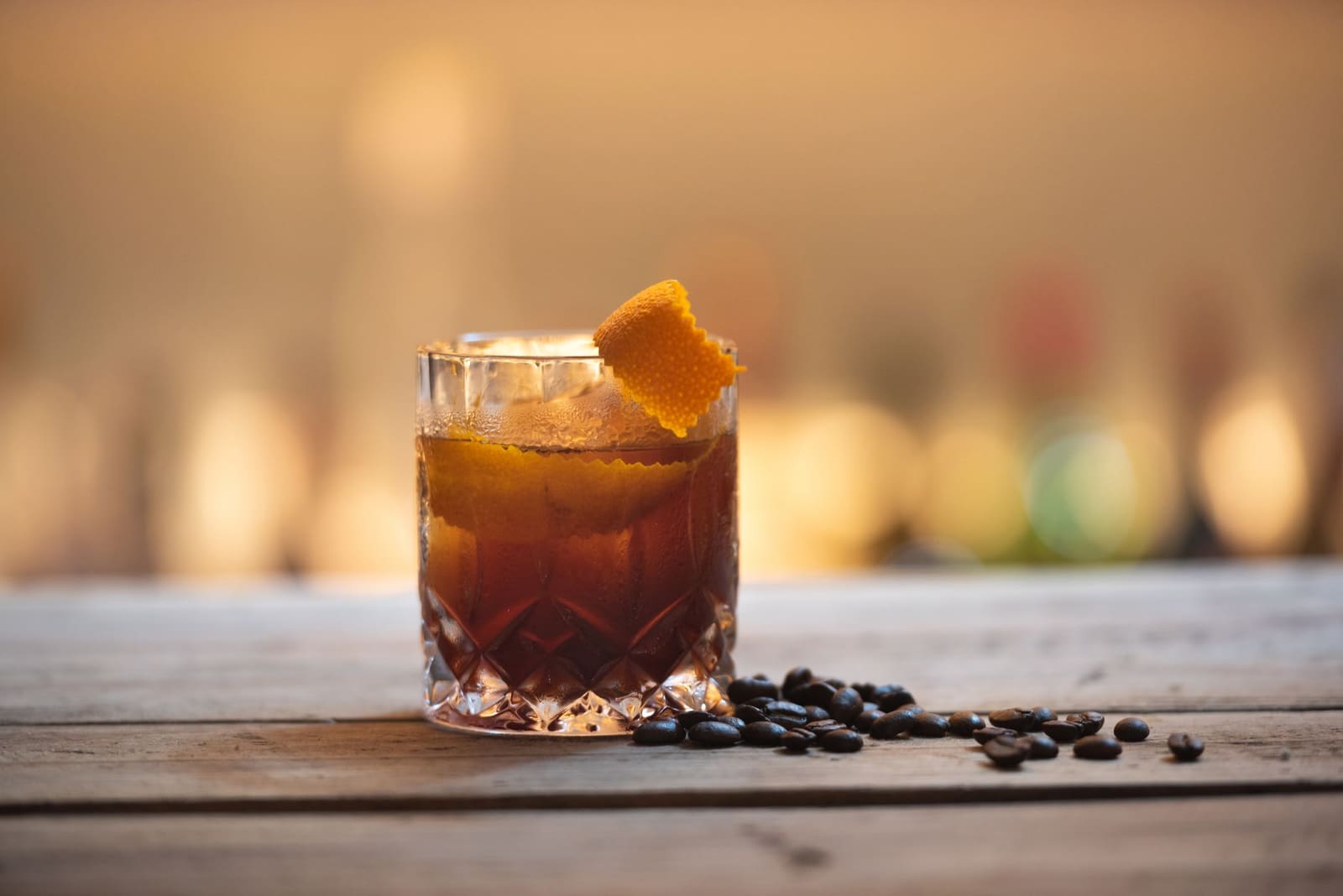 Oude fashioned cocktail met sinaasappelschil naast koffiebonen op houten bar