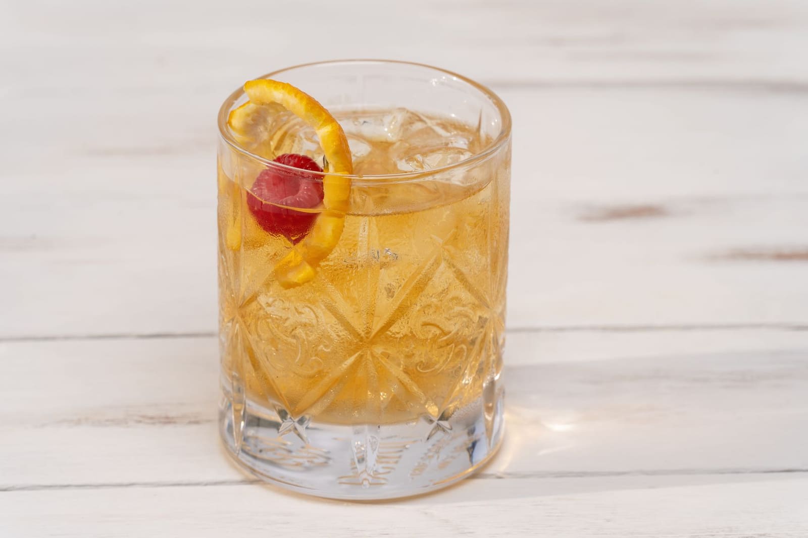 Een Amaretto Sour cocktail met schuimkraag en citrustwist op een houten bar