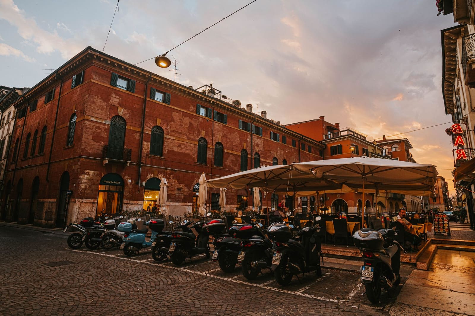 Piazza met cafétafels en stoelen in de avond, met oude gebouwen op de achtergrond.