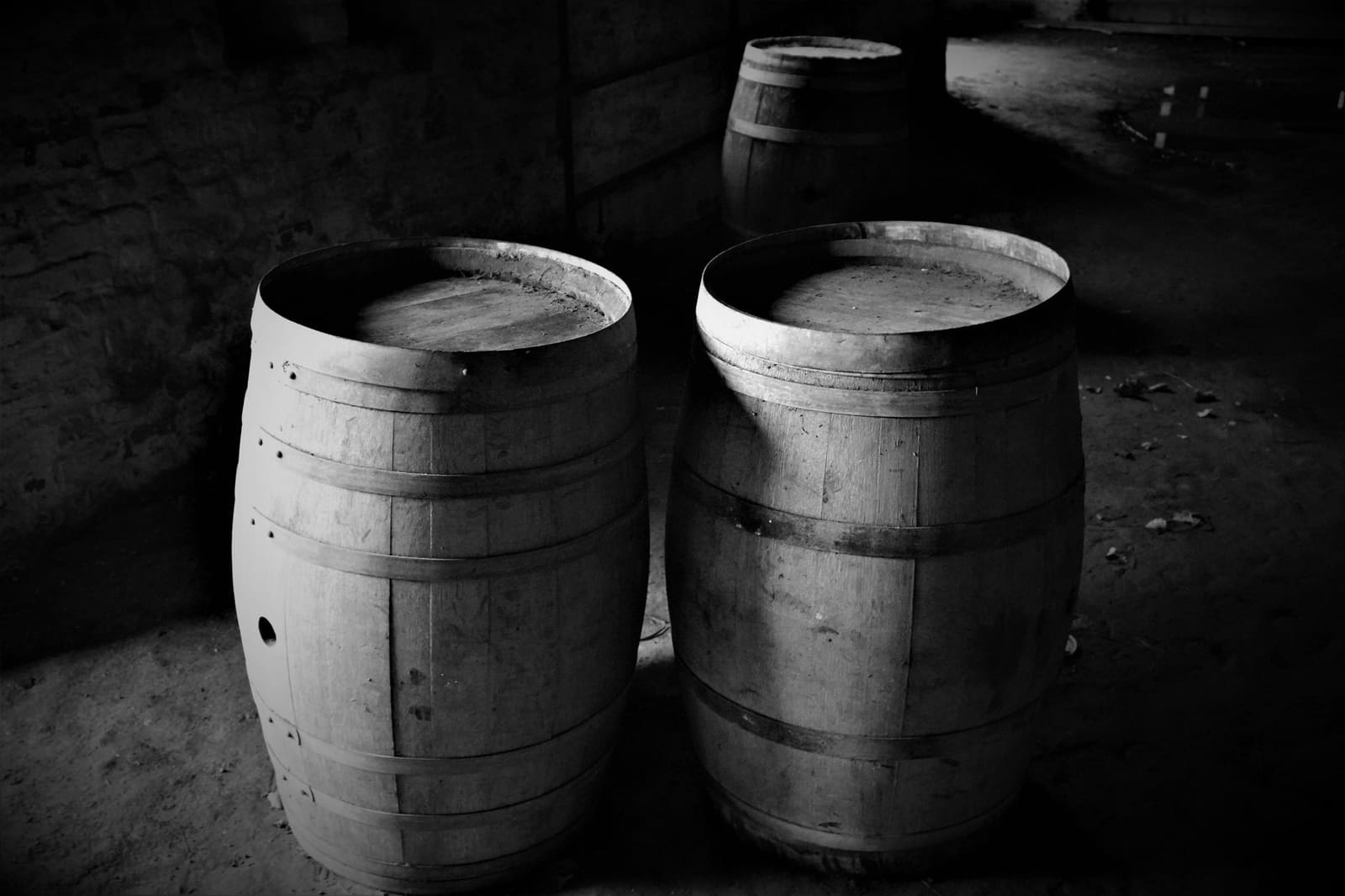 Houten whiskyvaten gestapeld in een donker magazijn, waar de whisky jarenlang rustig rijpt