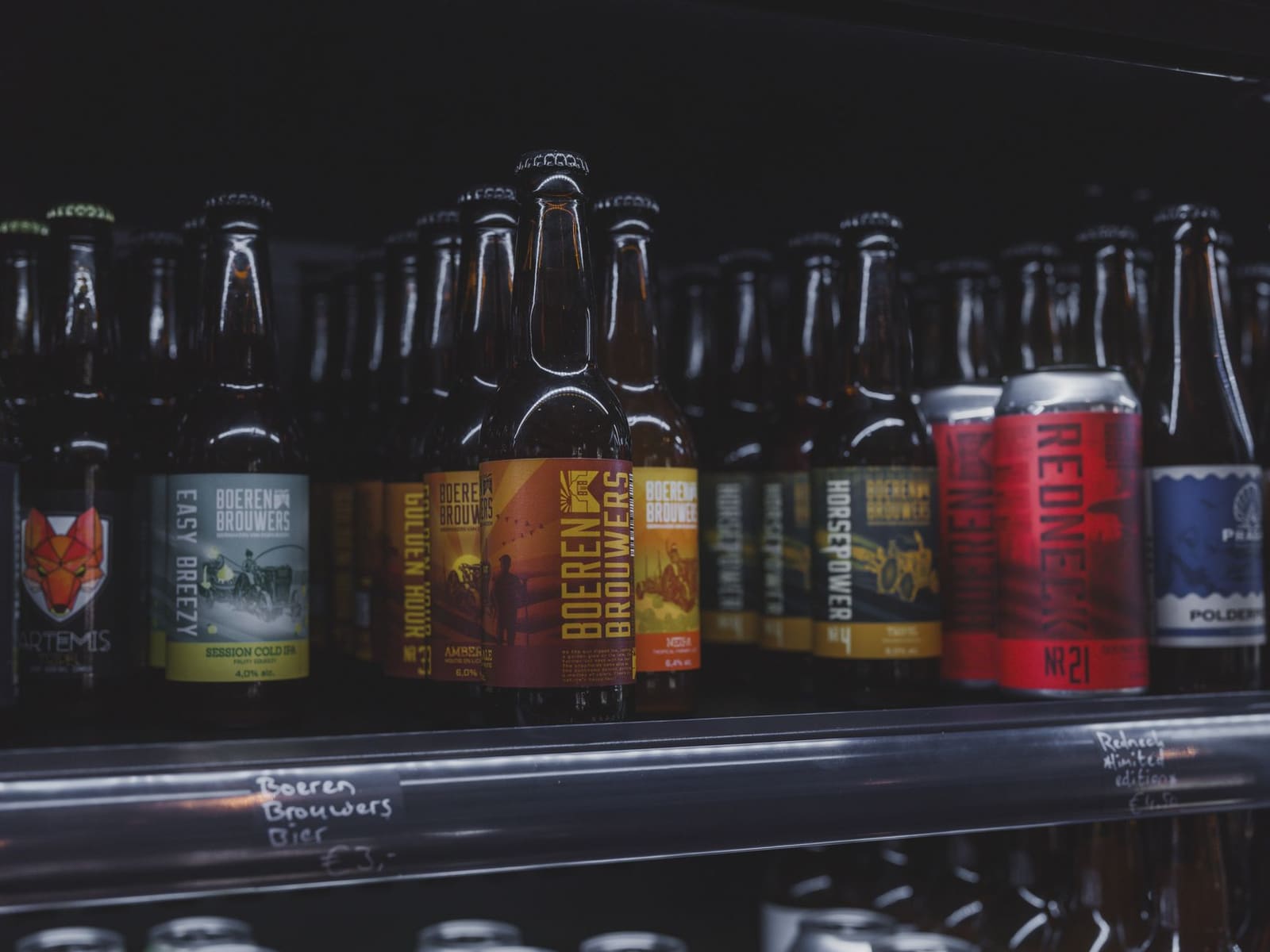 Rijen bierflesjes en blikjes uitgestald in de schappen van een winkel
