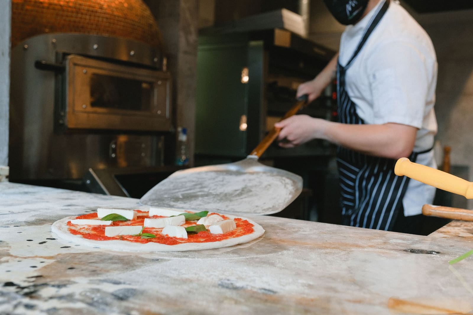 Pizzaiolo schuift een pizza met mozzarella en basilicum in de houtoven