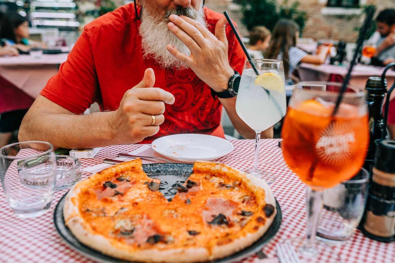 Man eet pizza aan tafel met twee cocktailglazen op geruit tafelkleed.