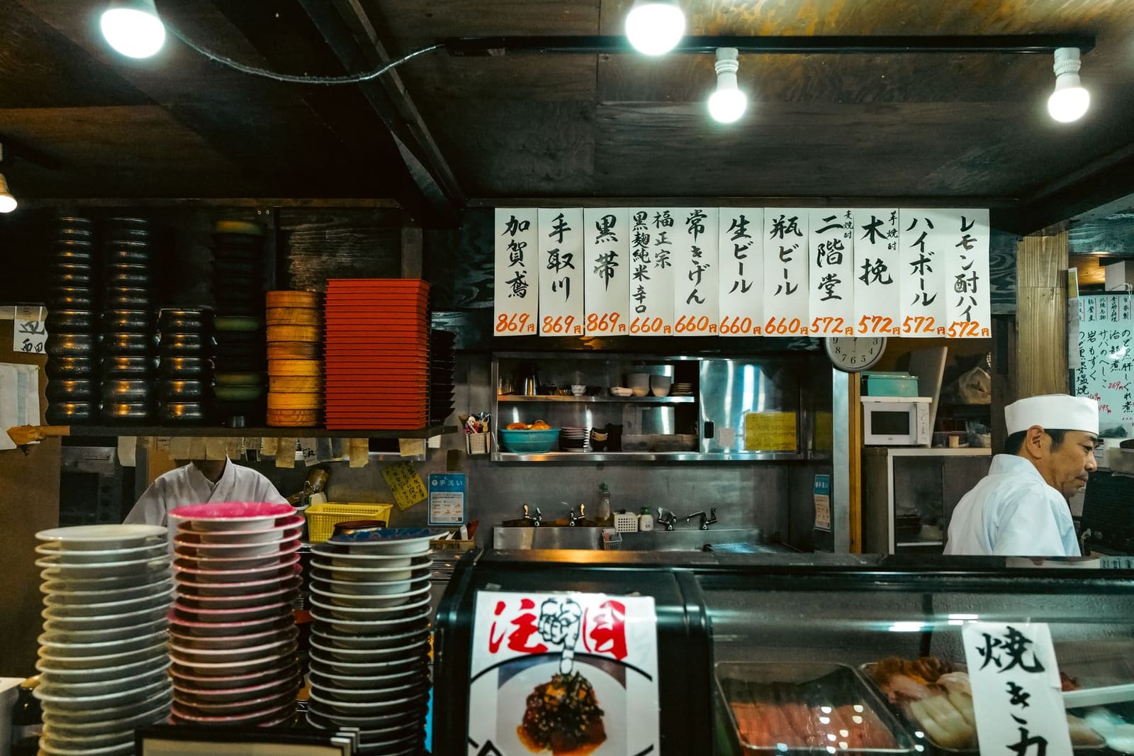 Lange houten bar in een Japans restaurant, met kleine lampen en zitplaatsen op rij.