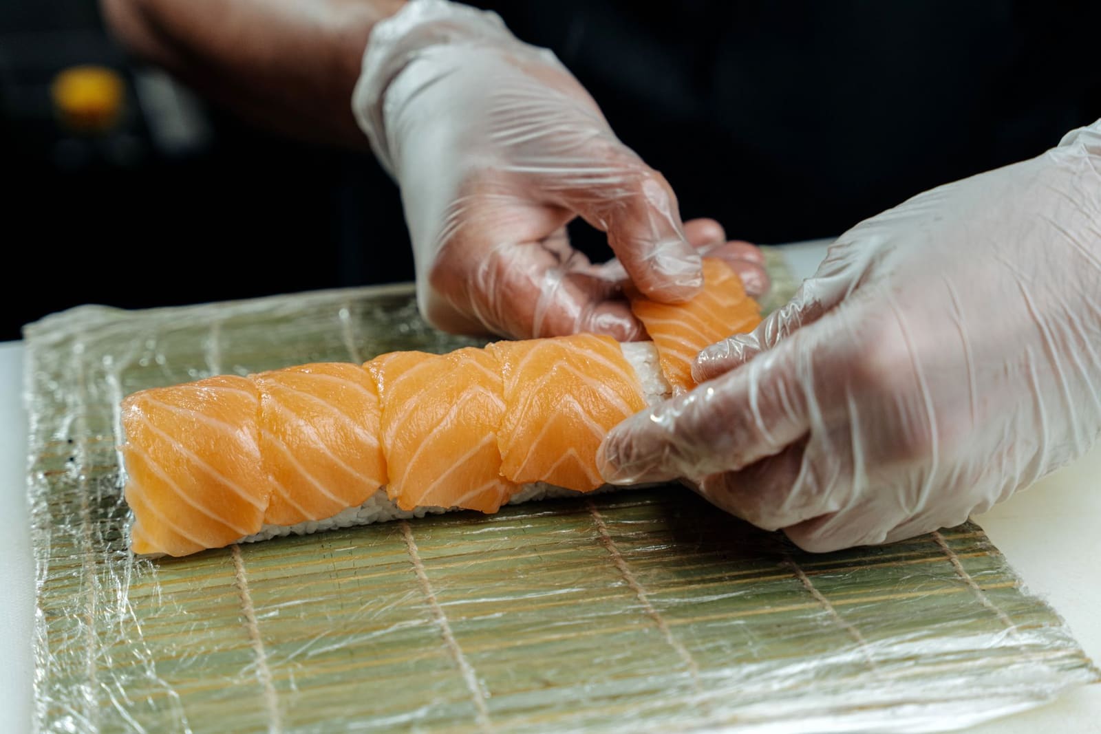 Sushikok rolt rijst en vis met de handen op een houten snijplank