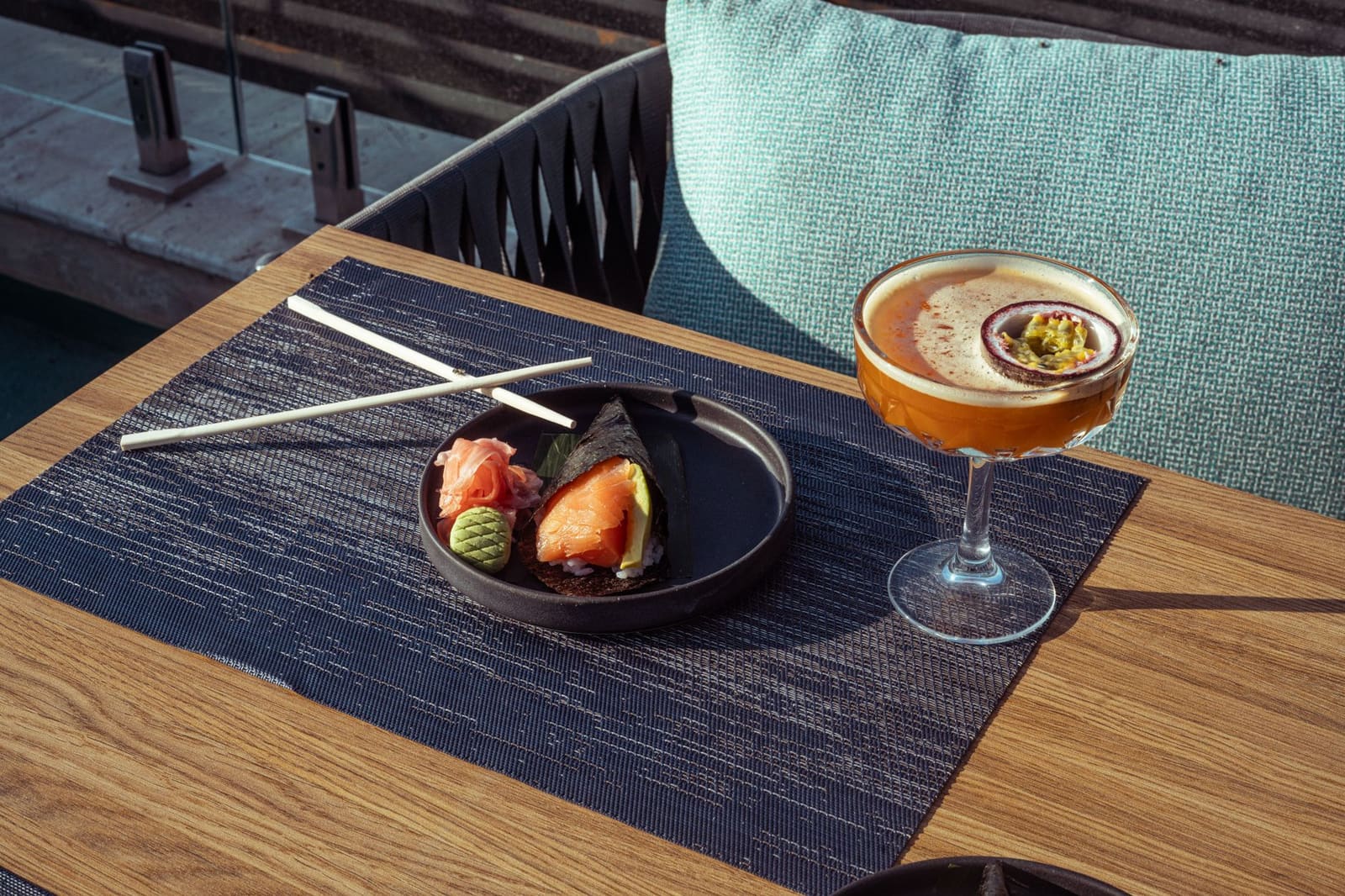 Sushi handroll met gember en wasabi naast een cocktail met passievrucht op terrastafel