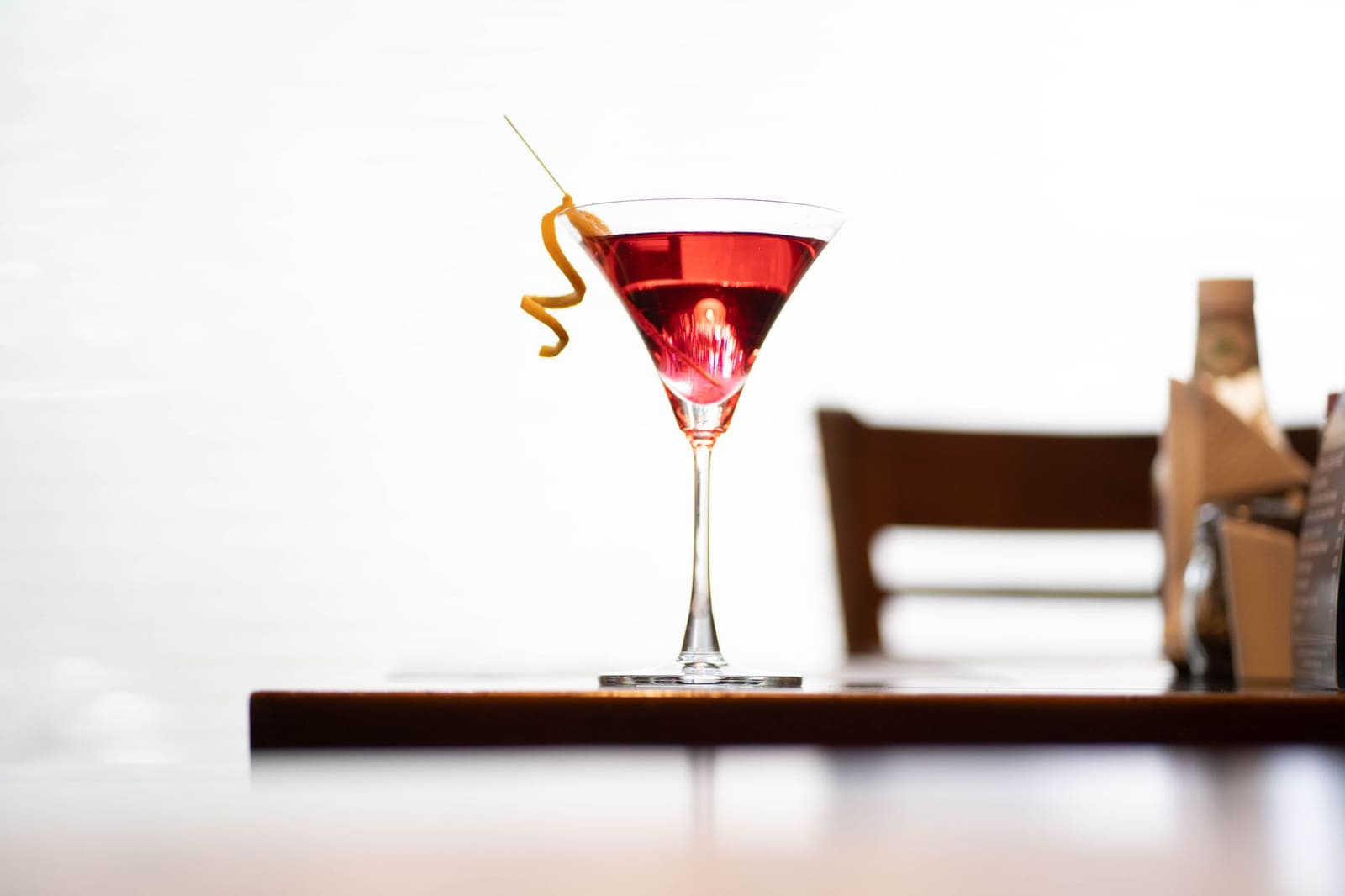 Gele citroenschil in een gedraaide spiraal naast een lege cocktailcoupe op een houten tafel