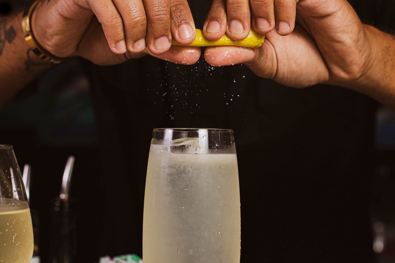 Bartender besprenkelt citroenschilbewerking boven cocktailglas met schuimende drank op bar