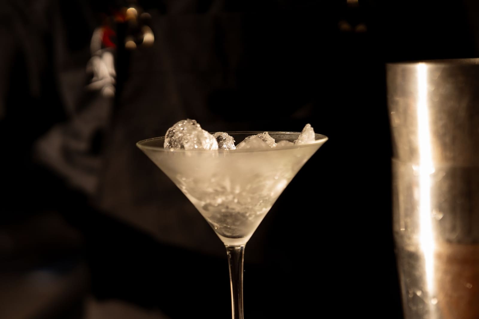 Metalen cocktail shaker met ijsblokjes en condens op een zwarte achtergrond.