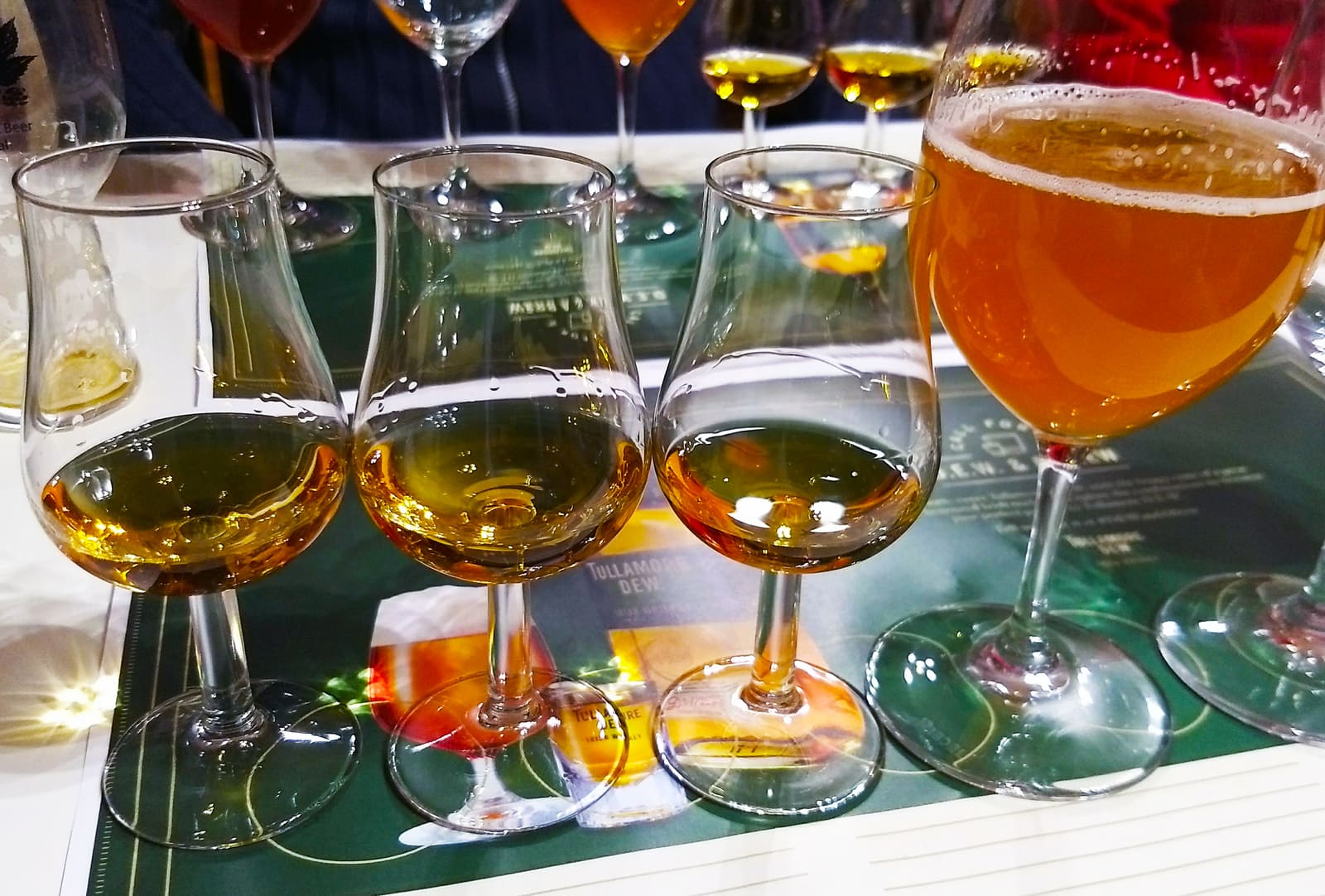Diverse whiskyglazen en een bierglas op een proeverijtafel met Tullamore Dew-menukaart.