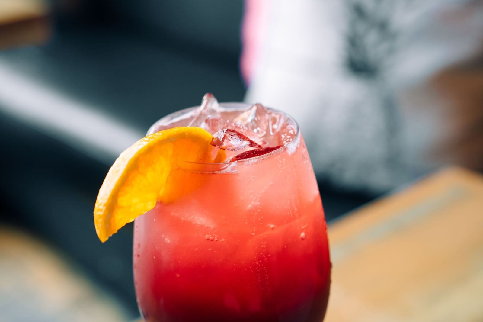 Een rode Negroni in een rocksglas met een groot ijsblok en sinaasappelschil