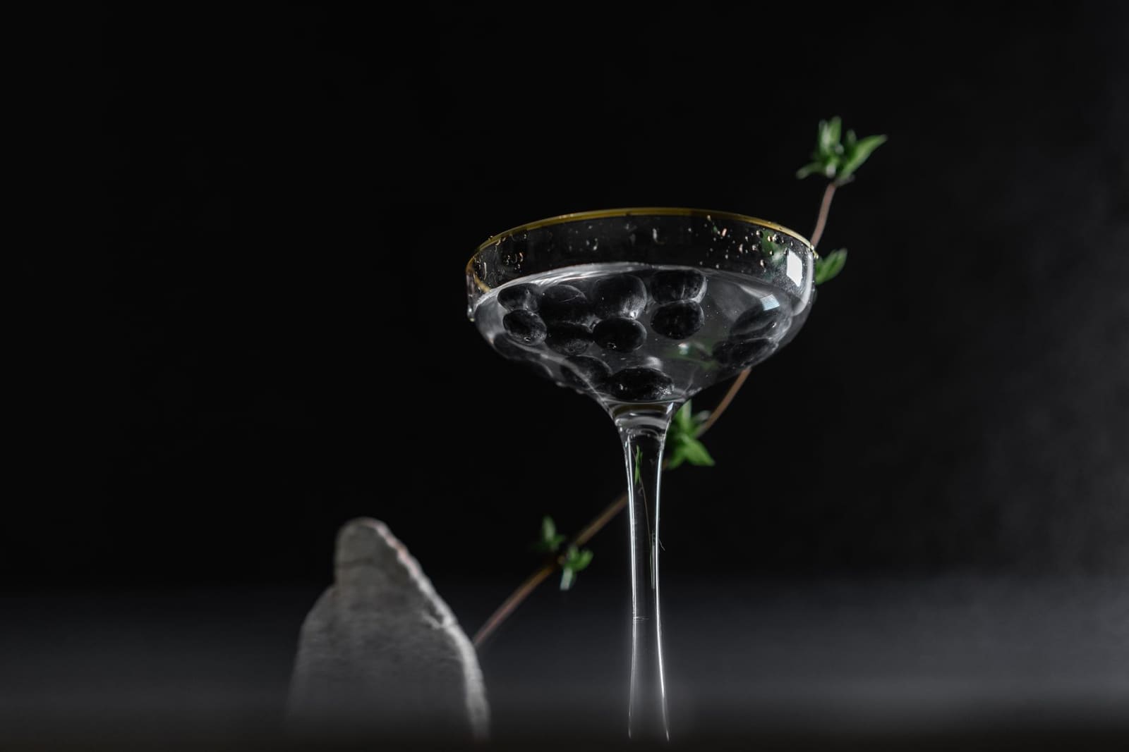 Een coupeglas met een lichte cocktail op een donkere bar, de smalle steel en brede schaal zichtbaar.