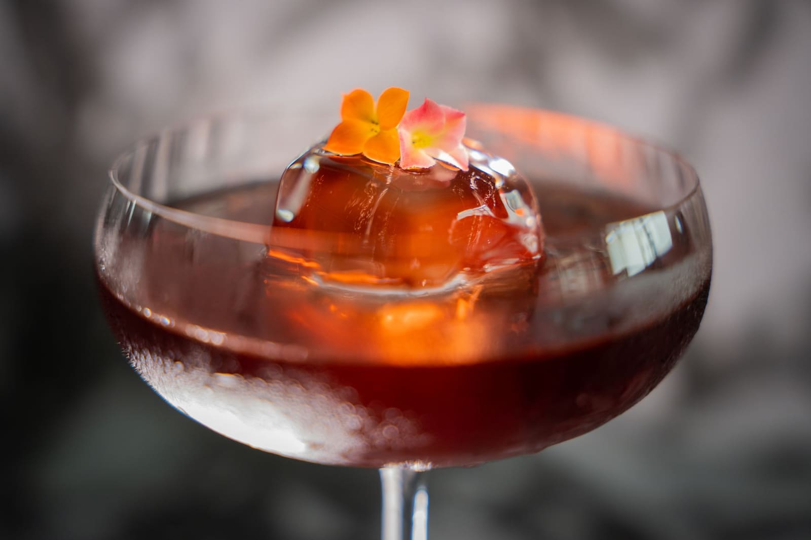 Een cocktail in een glas met ijsbol en bloemen als garnering, close-up.