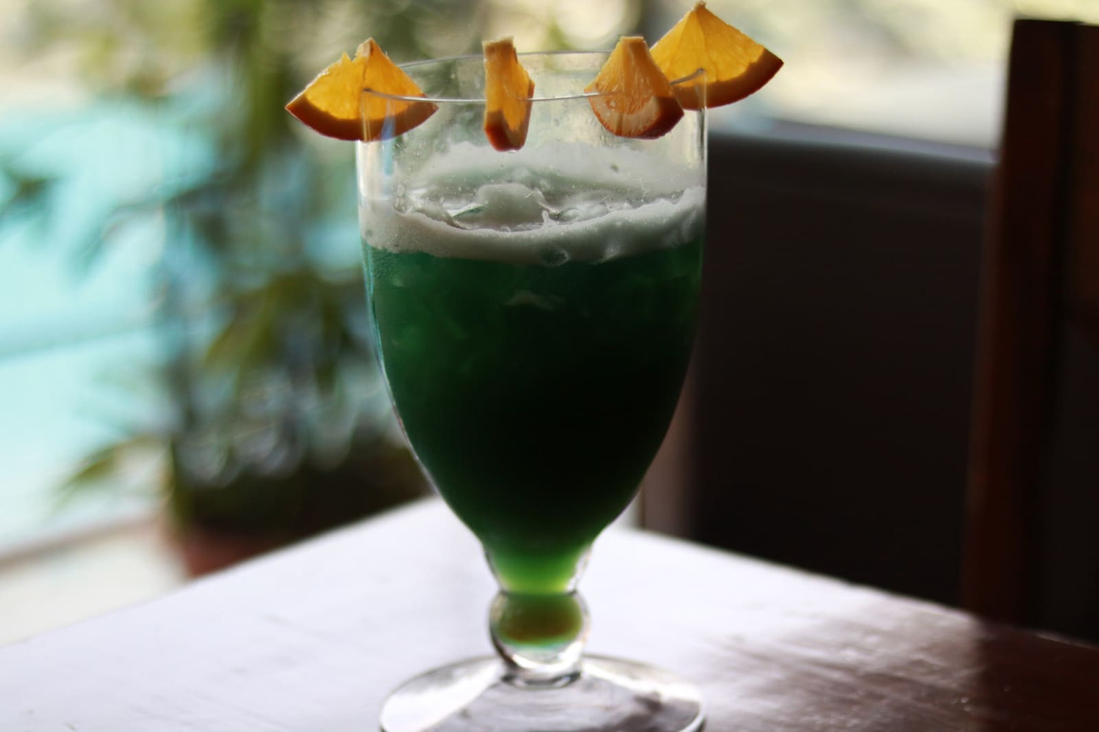 Felgroene cocktail met sinaasappelschijfjes in glas op tafel.