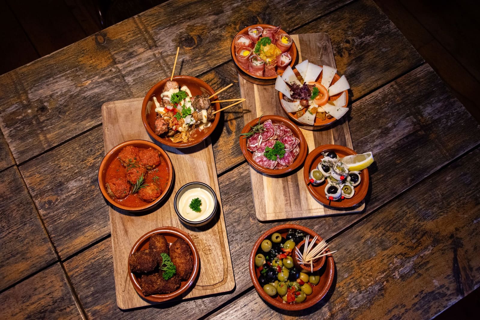 Schaal met olijven, chorizo en gebakken aardappel op een houten tafel in een Spaanse tapasbar.