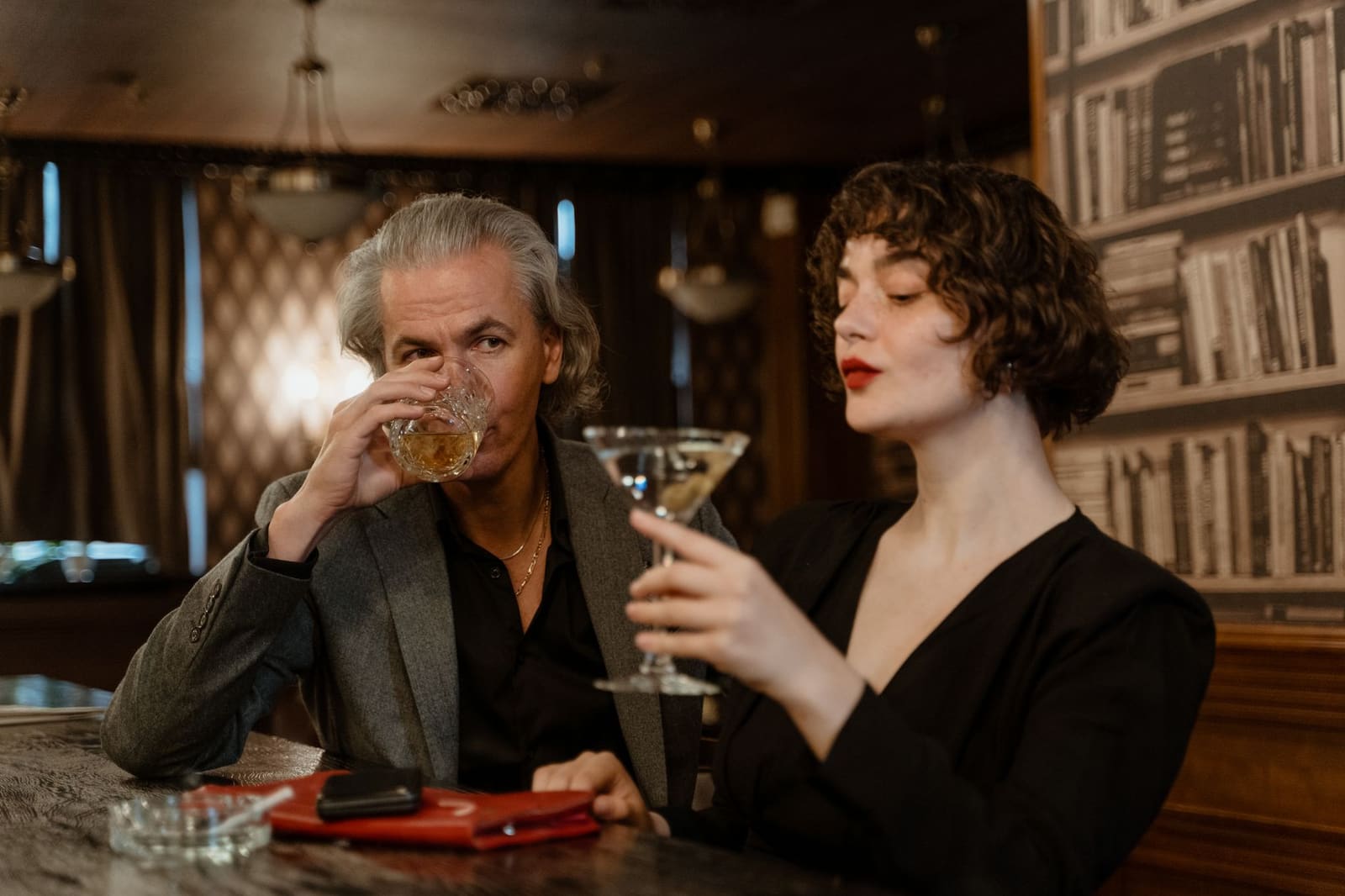 Gasten zitten in een gezellige cocktailbar met warm licht en lange bartafel