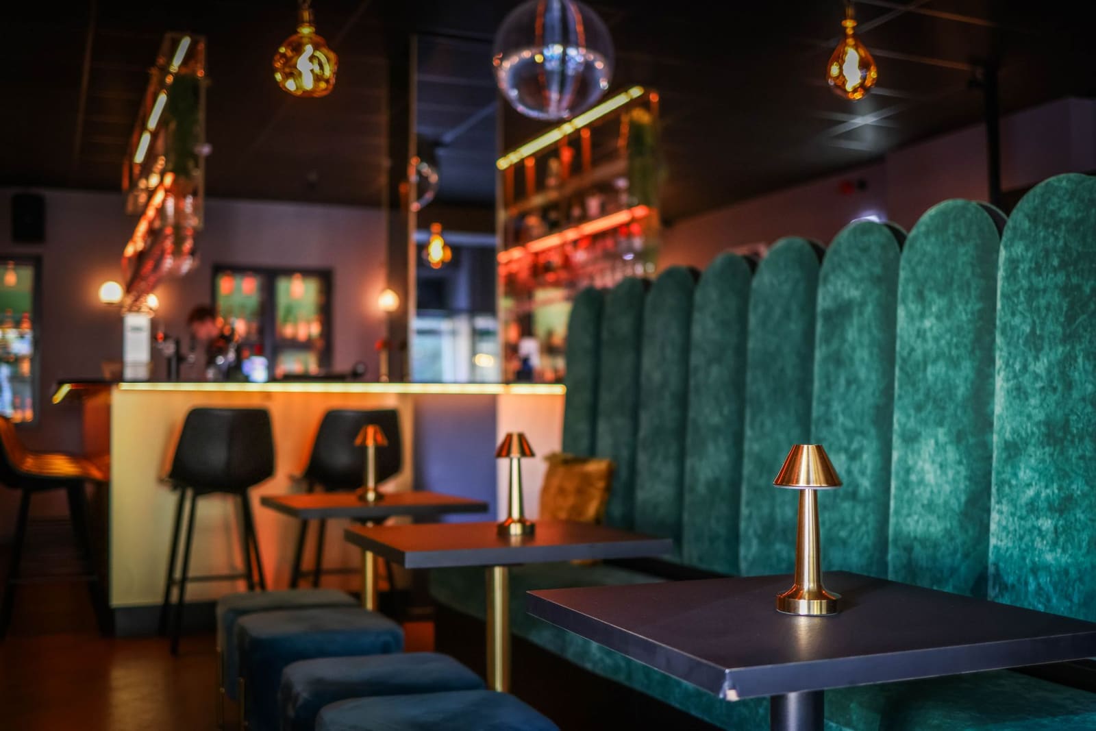 Sfeervol interieur van cocktailbar met groene fluwelen banken en tafellampjes.
