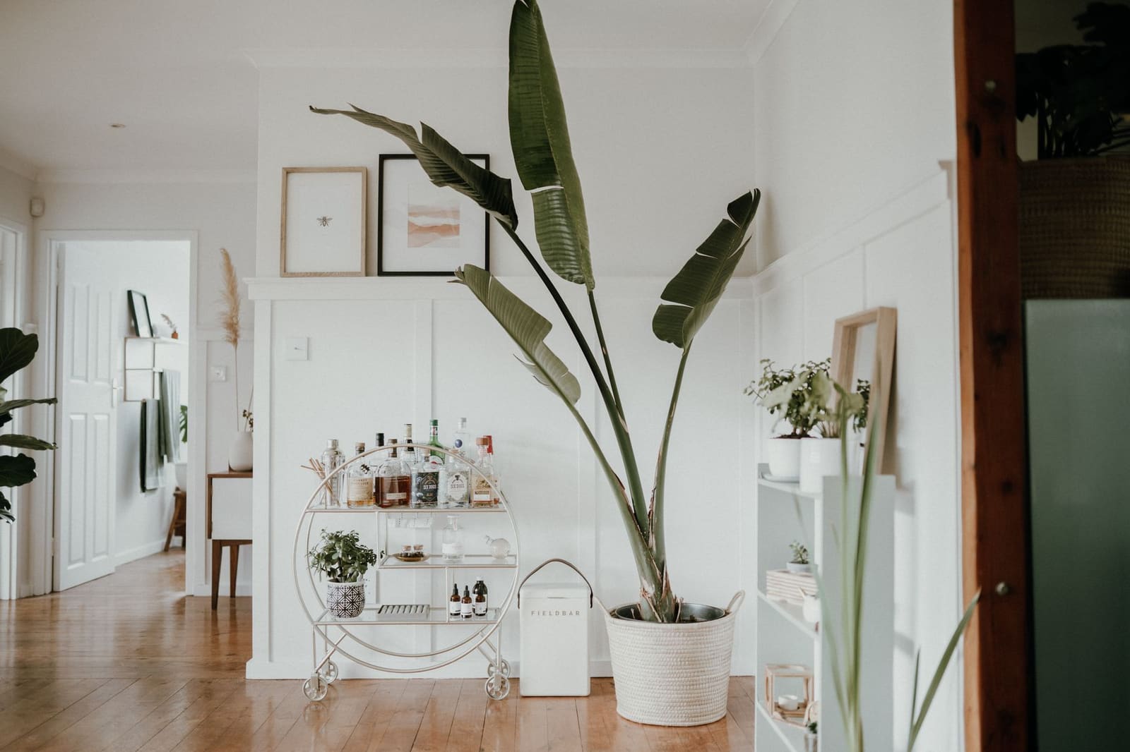 Thuisbar met flessen, glazen en een houten kastje in een huiskamer bij avondlicht.