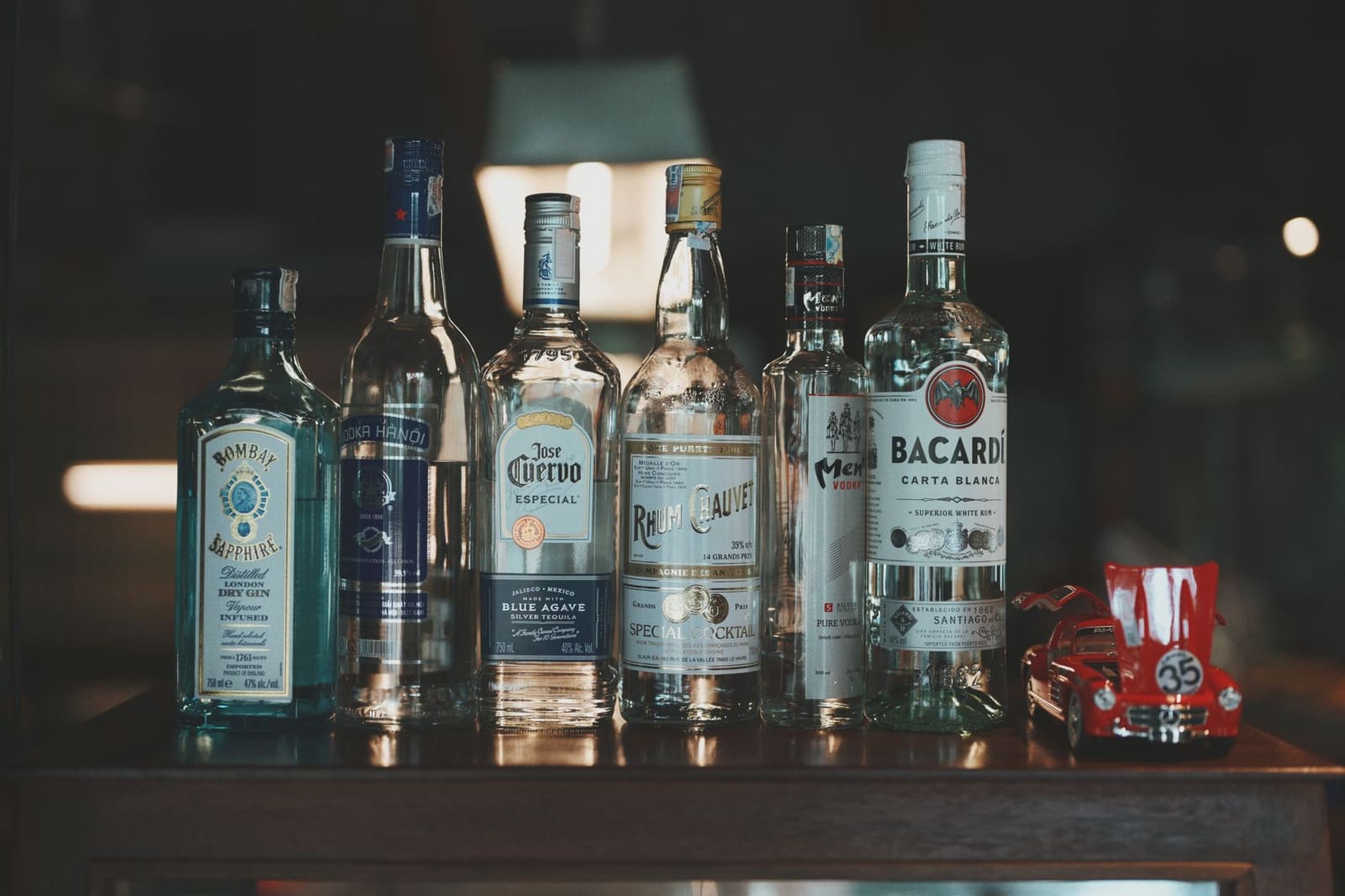 Flessen witte rum en gin staan op een donkere barkast achter de bar.