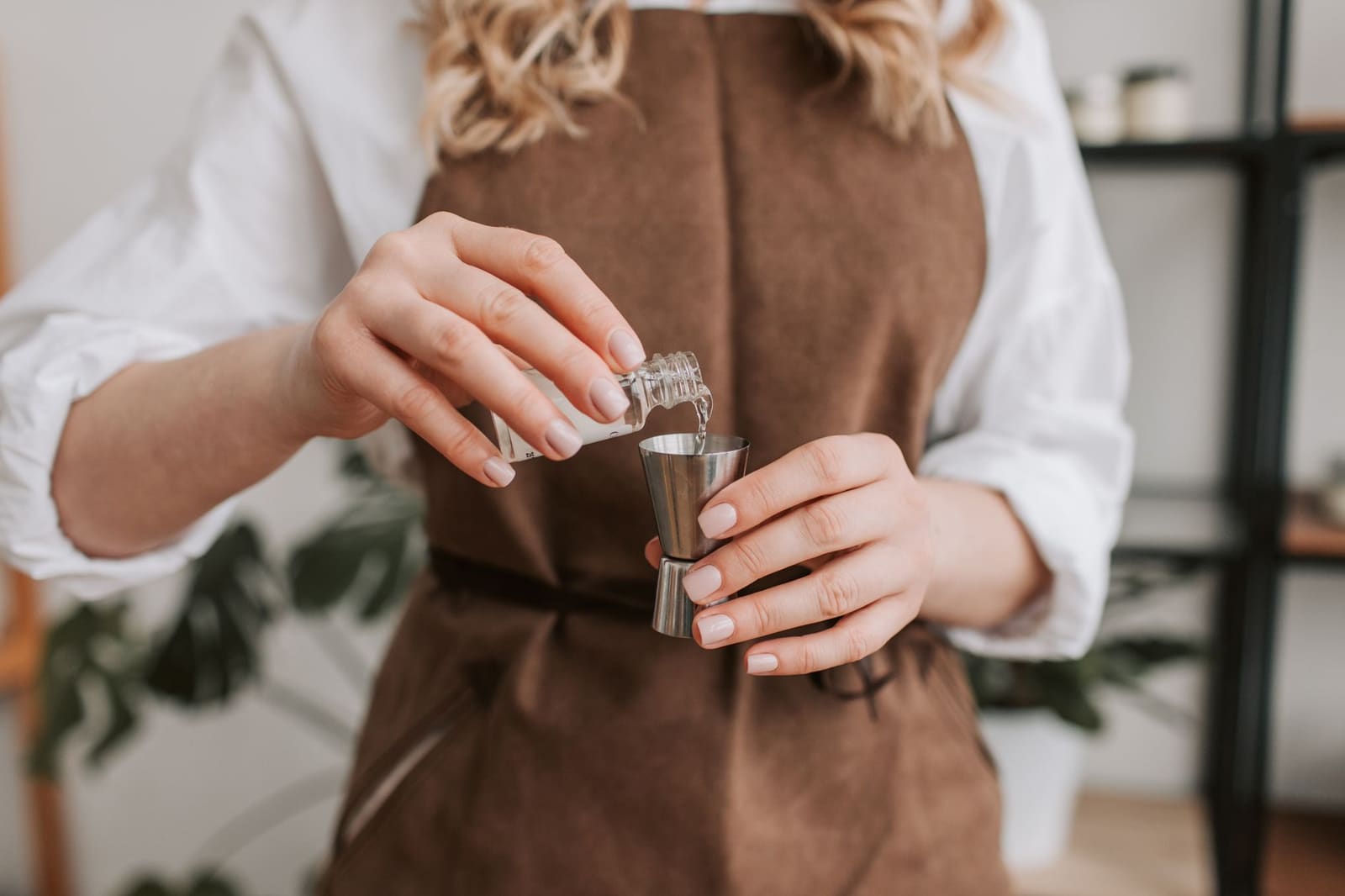 Een koperen jigger vol heldere sterke drank staat naast een cocktailglas op de bar.