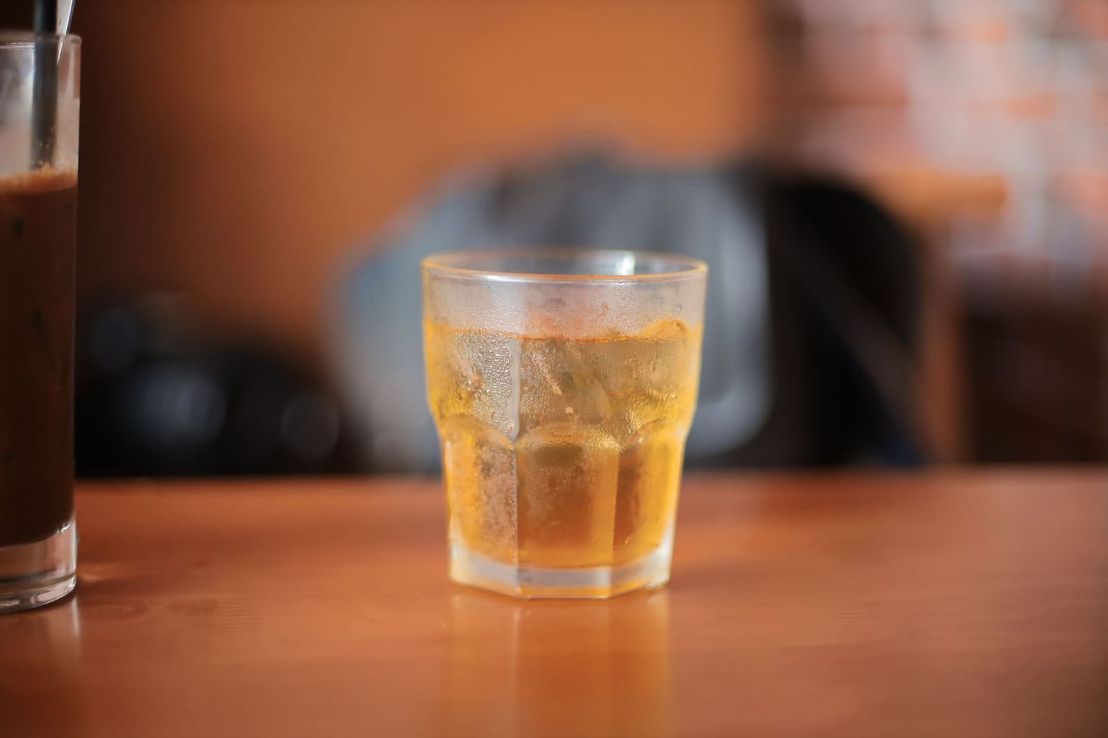 Amberkleurige whiskey in een tumbler met een groot ijsblok op een houten tafel.
