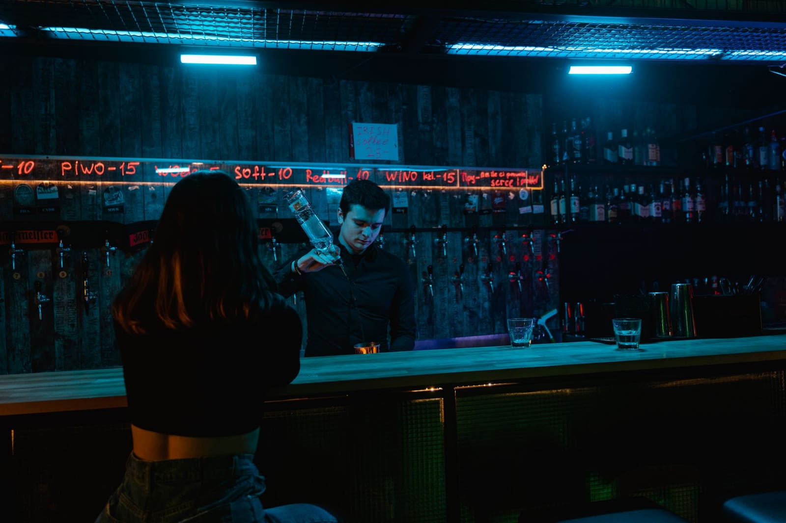 Barman schenkt een drankje in op een drukke bar met gasten op de achtergrond.