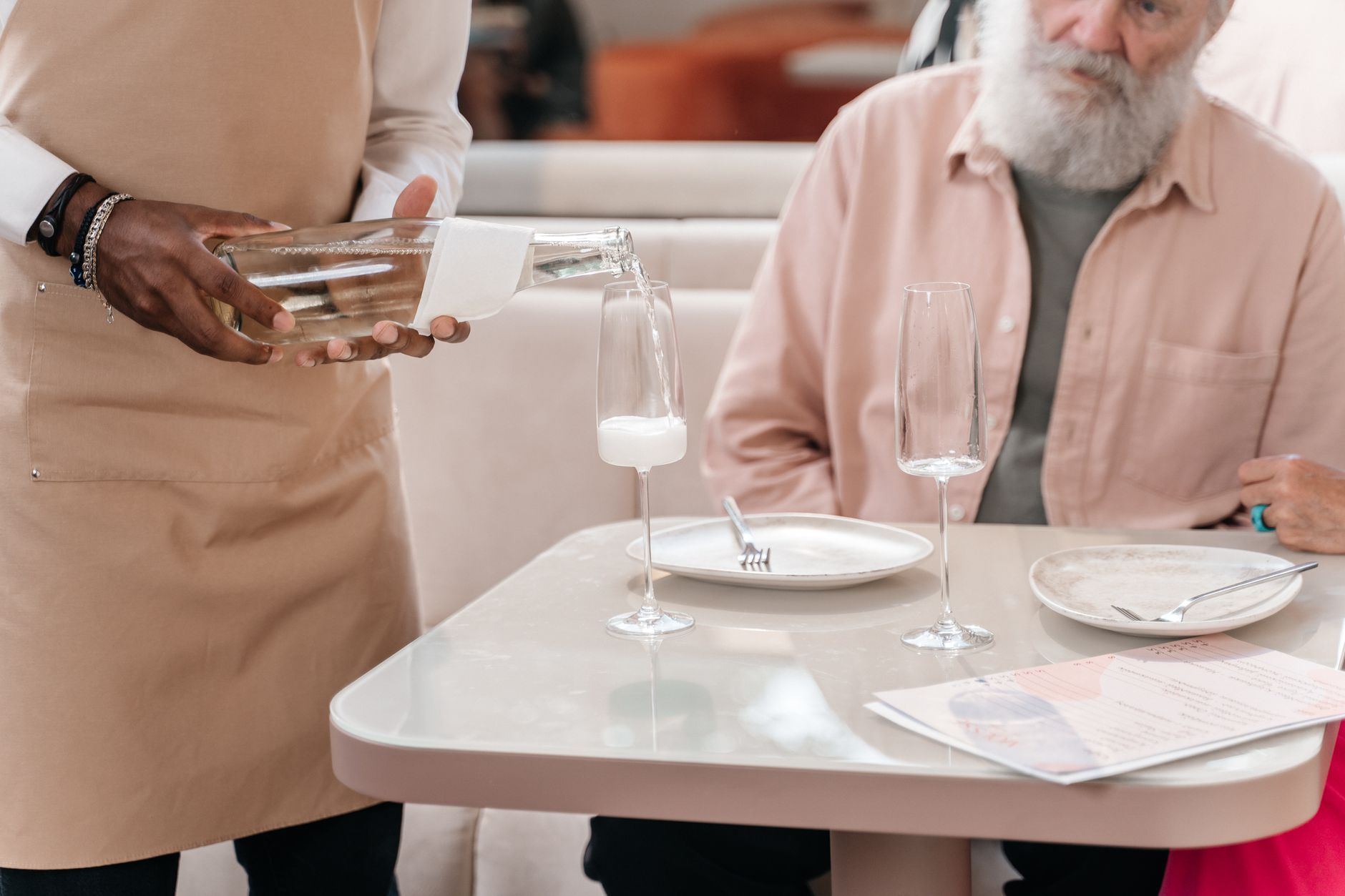 Ober schenkt witte wijn in een restaurant terwijl gasten aan tafel de sfeer opnemen