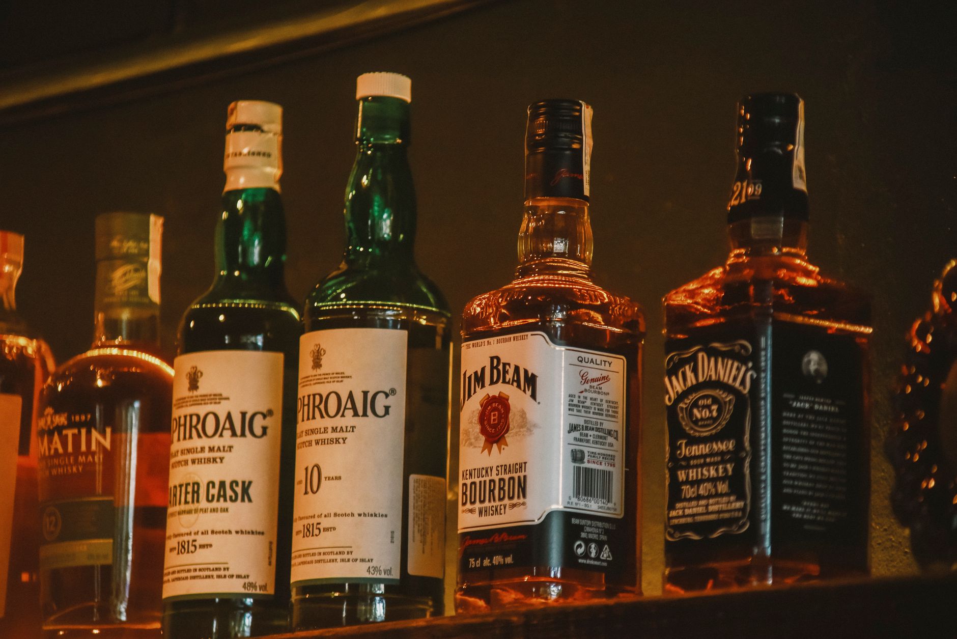 Rijen flessen whiskey, gin en vodka op een bar-schap, symbool voor de internationale drankindustrie