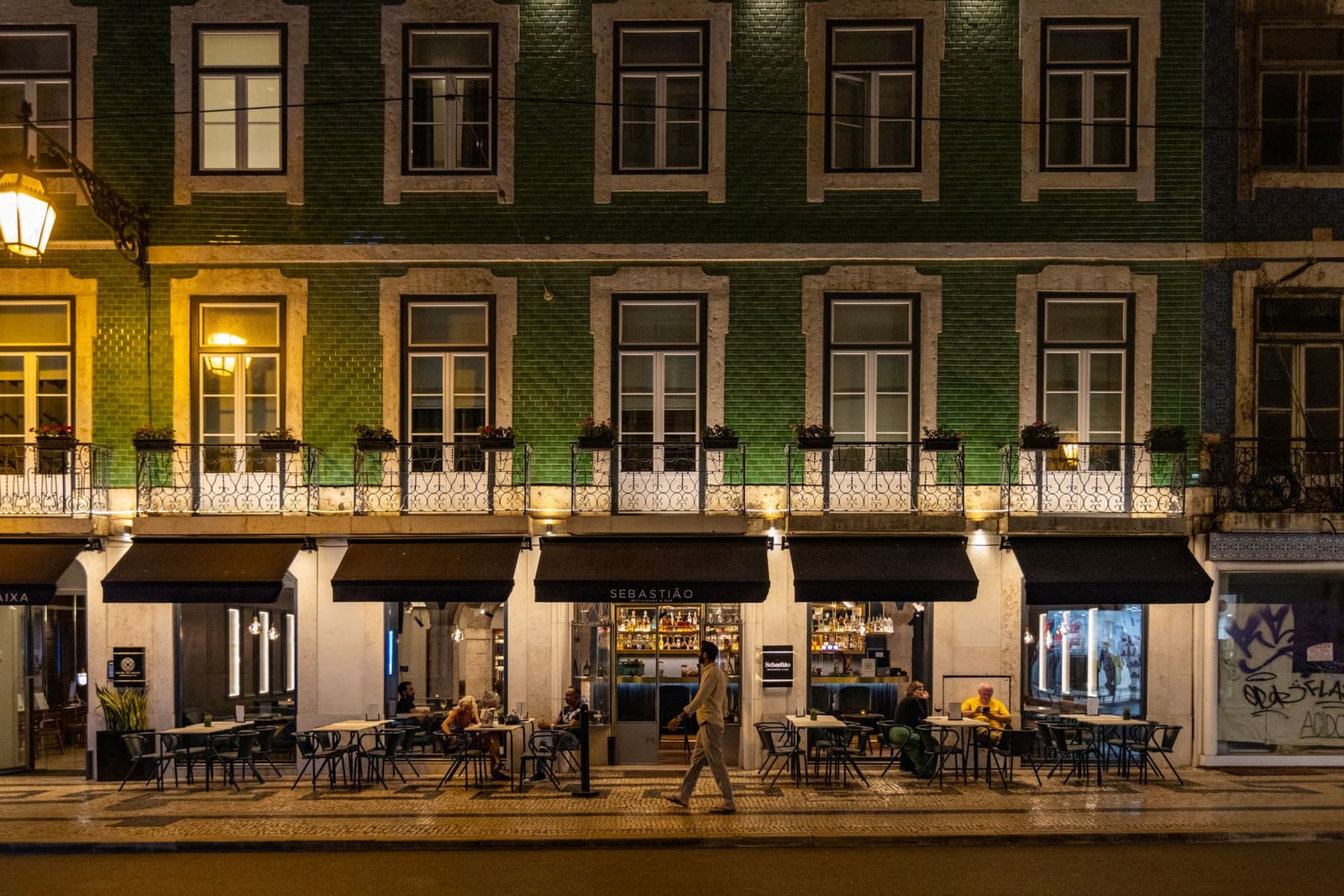 Verlichte straat in Lissabon met terras van restaurant Sebastião bij avond.
