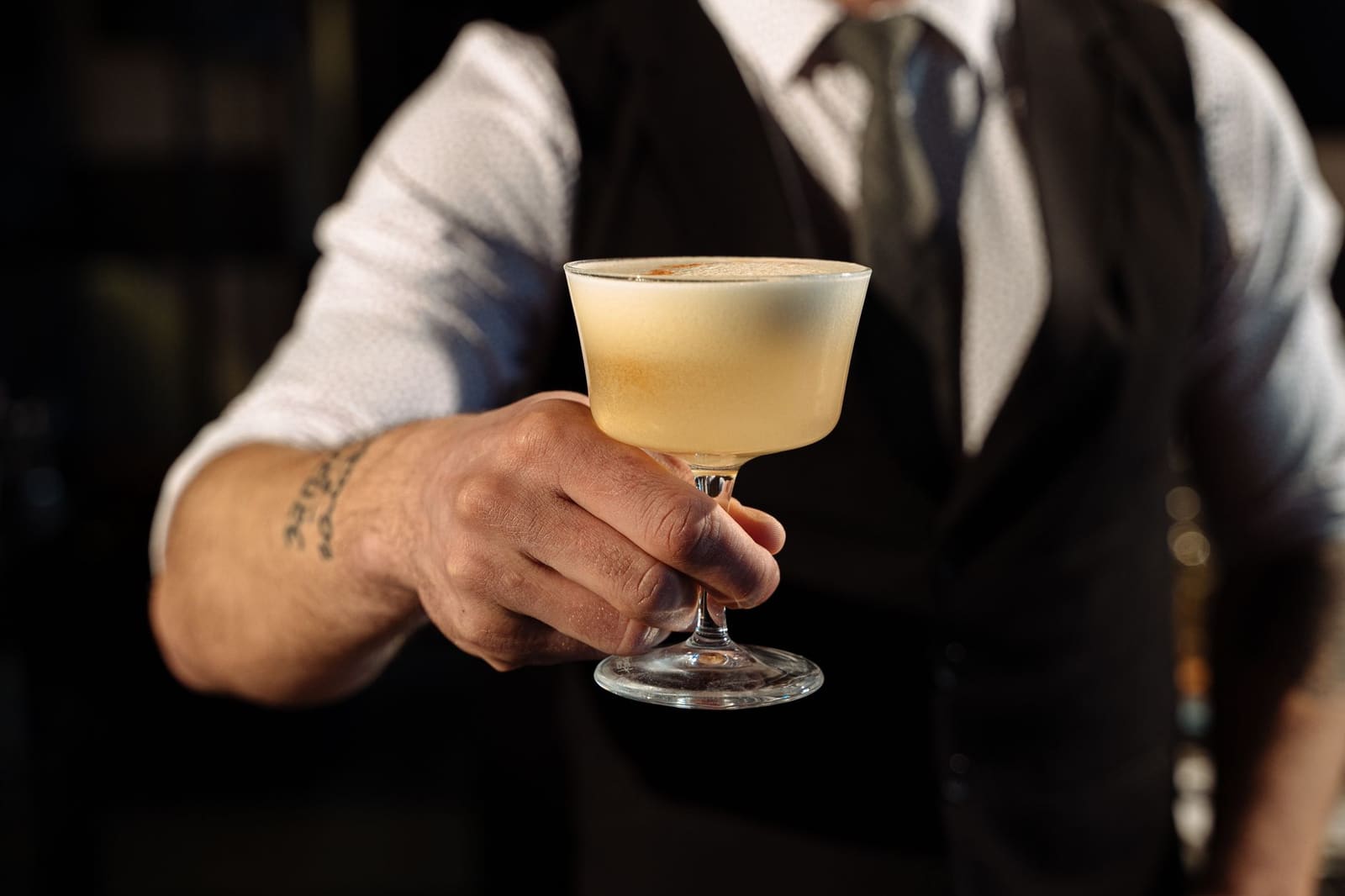 Een glas cocktail met een dikke laag wit schuim bovenop, geserveerd in een coupeglas.