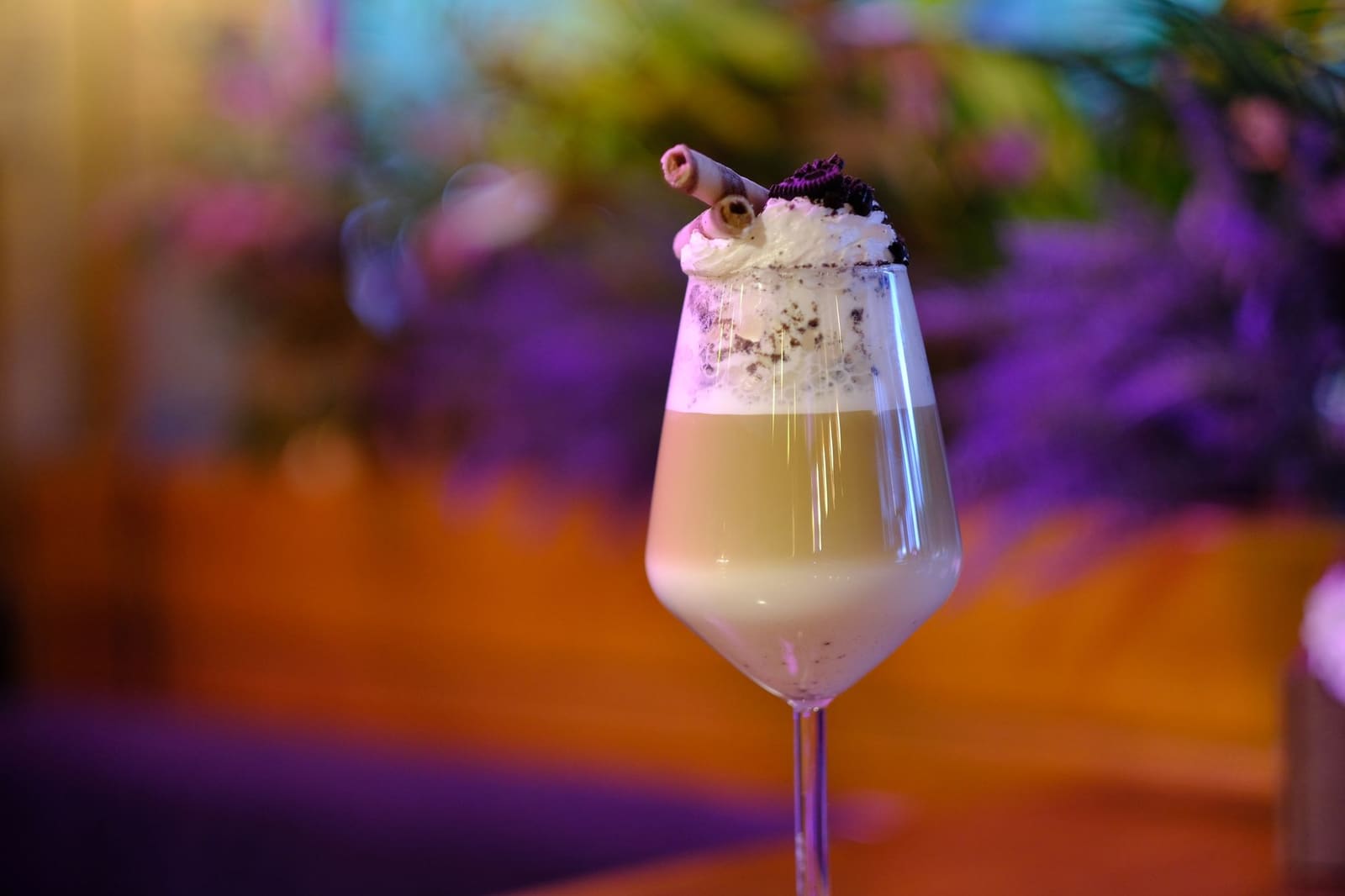 Cocktailglas met koffiekleurige drank, slagroom, koekjeskruim en wafelrolletjes als decoratie.