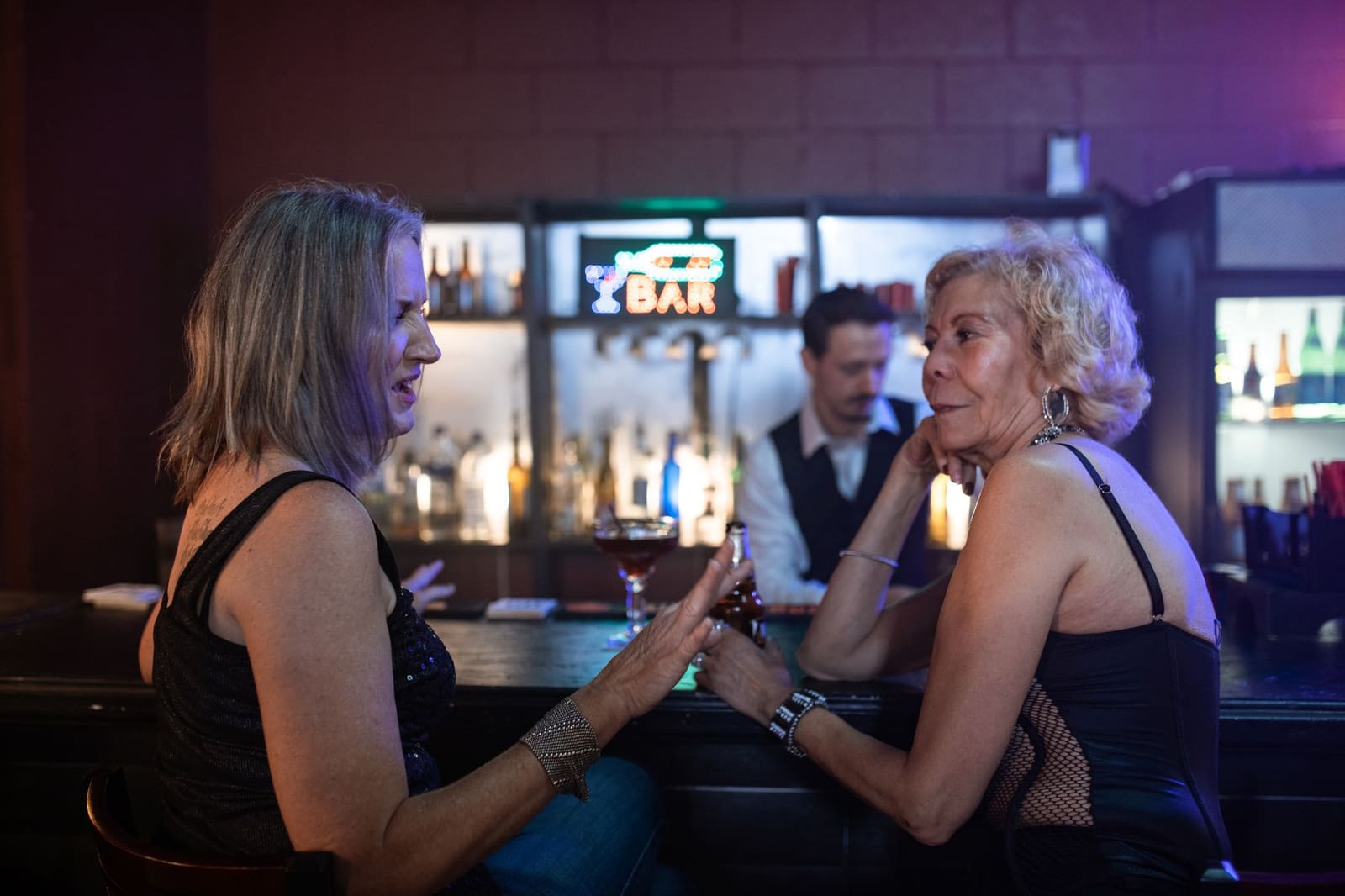 Vrouwelijke barmedewerkers staan lachend achter een bar met flessen in het rek.