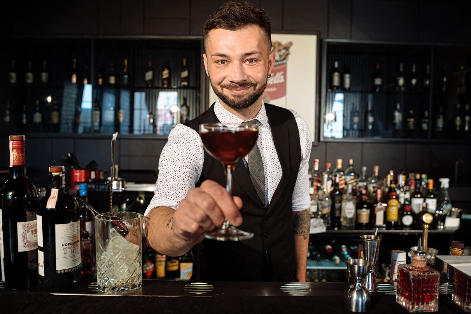 Bartender houdt een munt vast achter de bar, met flessen op de achtergrond.