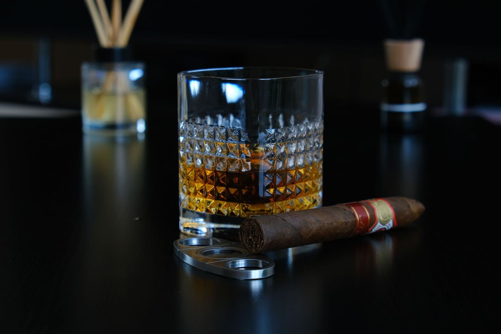 Glas whisky met sigaar en sigarenknipper op donkere houten tafel.