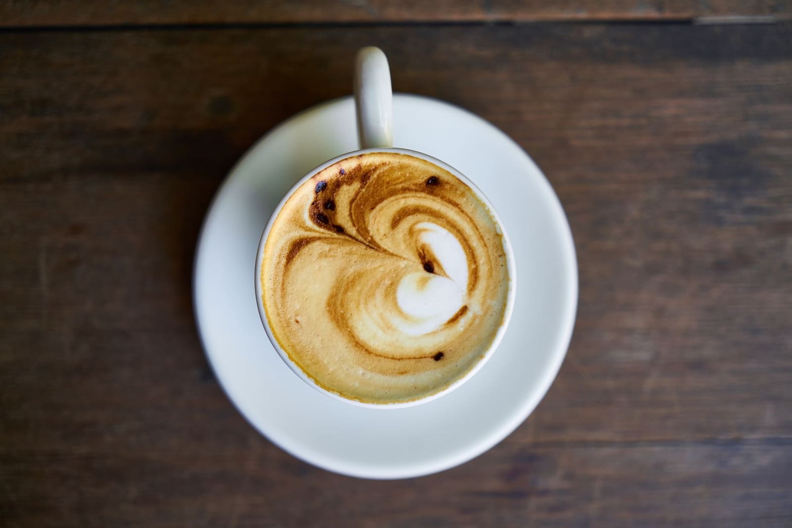 Cappuccino met melkschuim en latte art in een wit kopje op een houten tafel