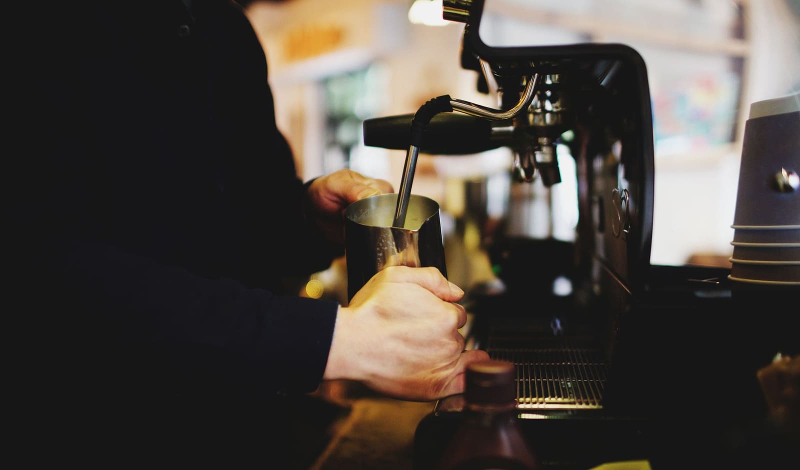 Close-up van een barista die melk opschuimt bij een espressomachine achter de bar.