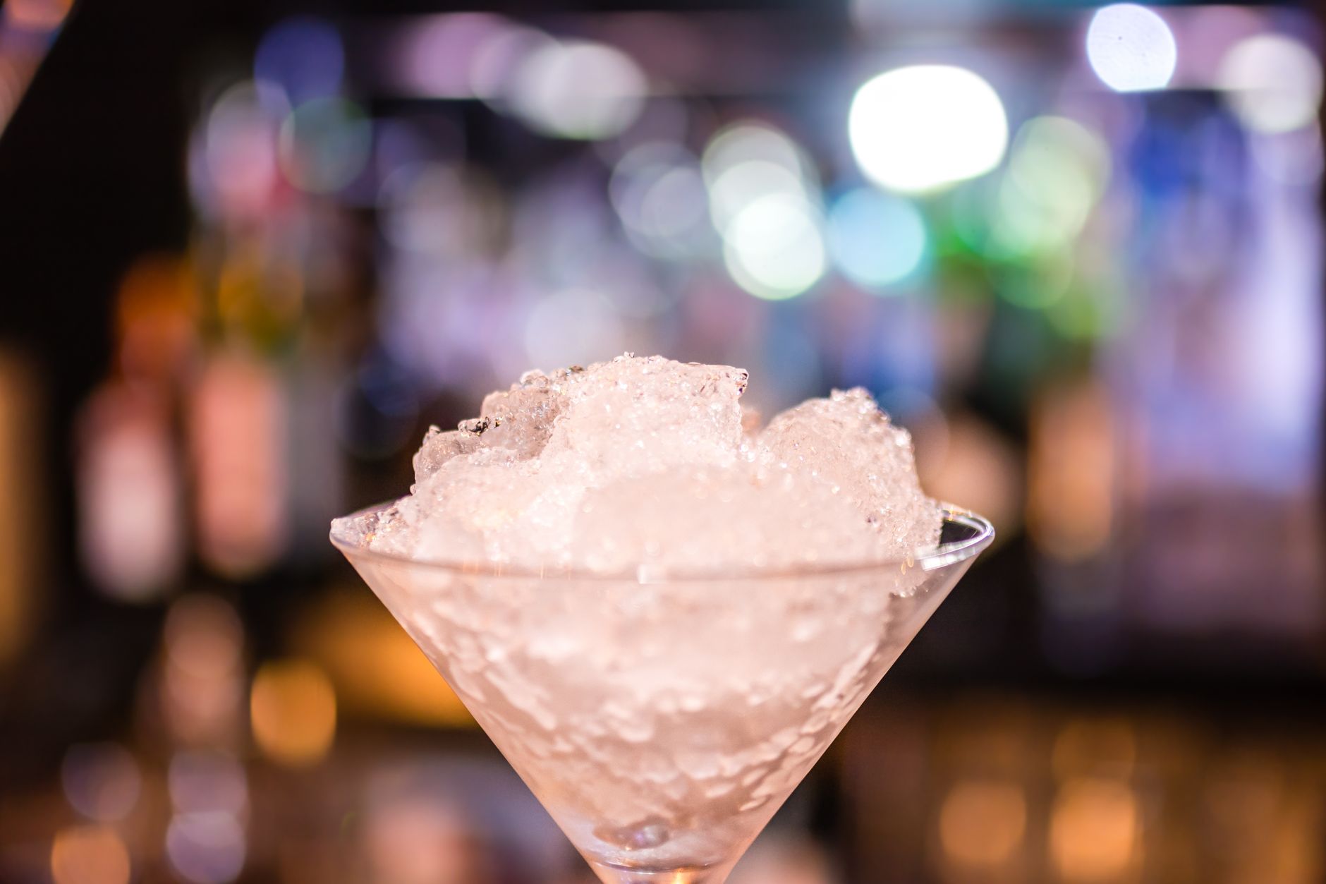 Bartender schaaft ijs van een groot blok tot een luchtige berg geraspt ijs voor een cocktail