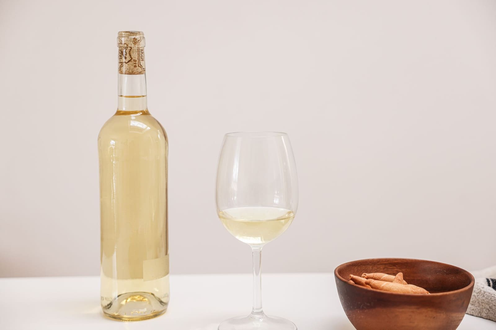 Fles witte wijn zonder etiket naast een gevuld wijnglas op tafel