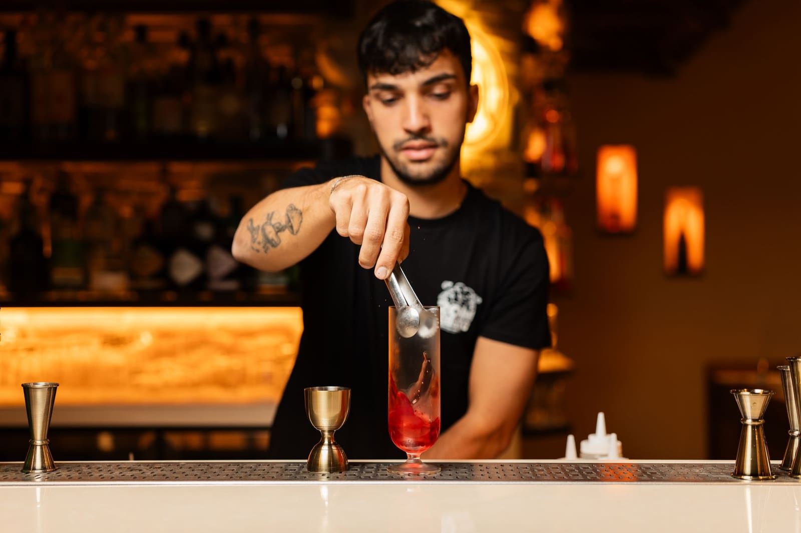 Bartender die een cocktail shaket achter een druk verlichte bar