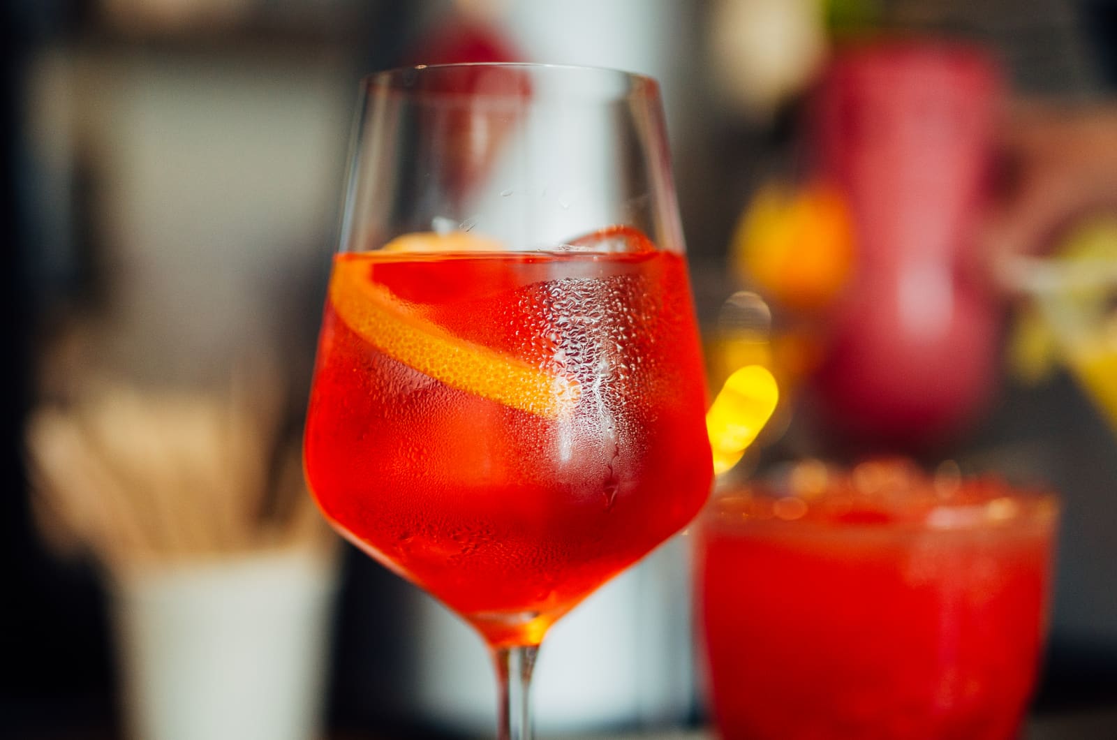 Close-up van een rood aperitiefcocktailglas met sinaasappelschil, roomijs en flessen op achtergrond.