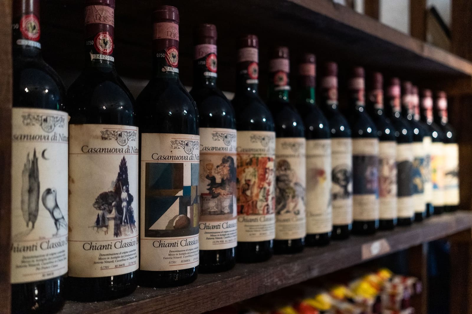 Rij flessen Chianti Classico wijn met etiketten op houten wijnrek.