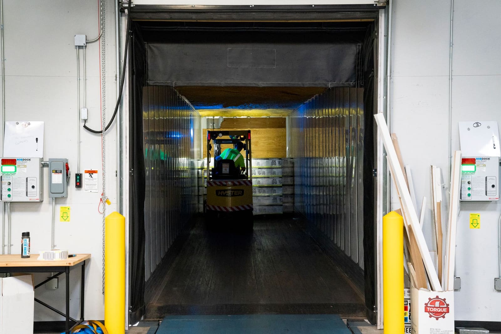 Vrouw in een magazijn met een heftruck tussen de pallets