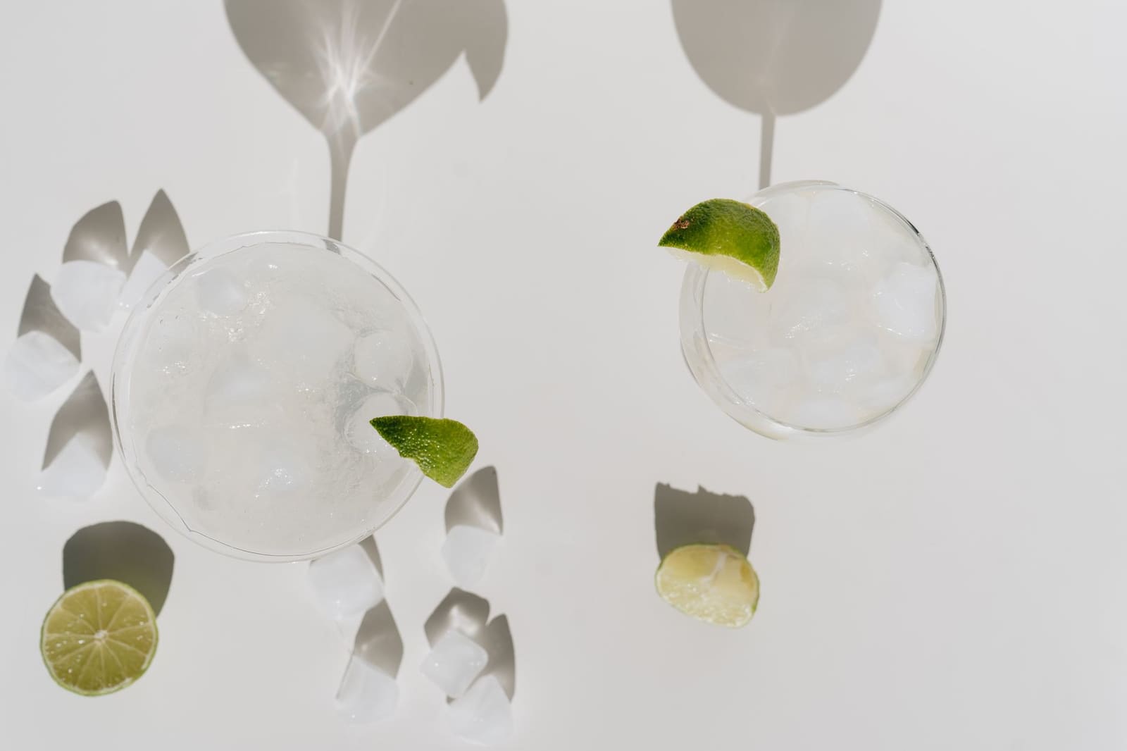 Twee cocktails met ijsblokjes en limoen, bovenaanzicht op witte achtergrond