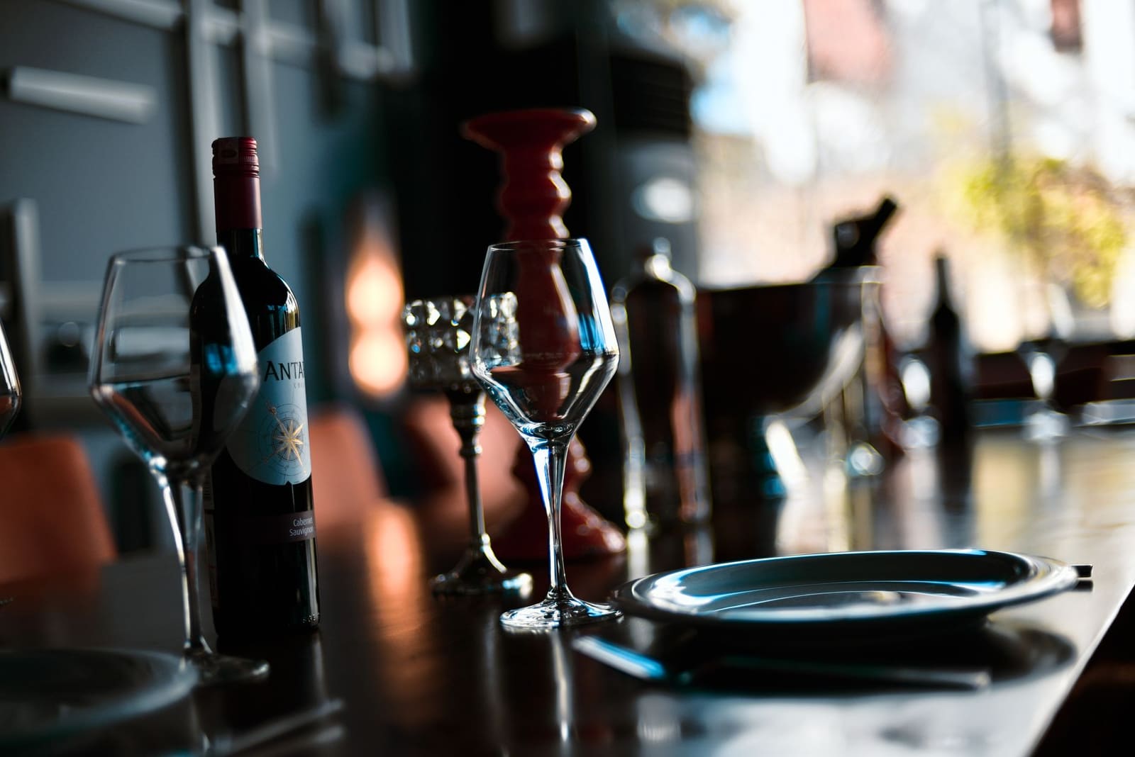 Gedekte restauranttafel met wijnglazen, wijnfles en kandelaar in avondsfeer.