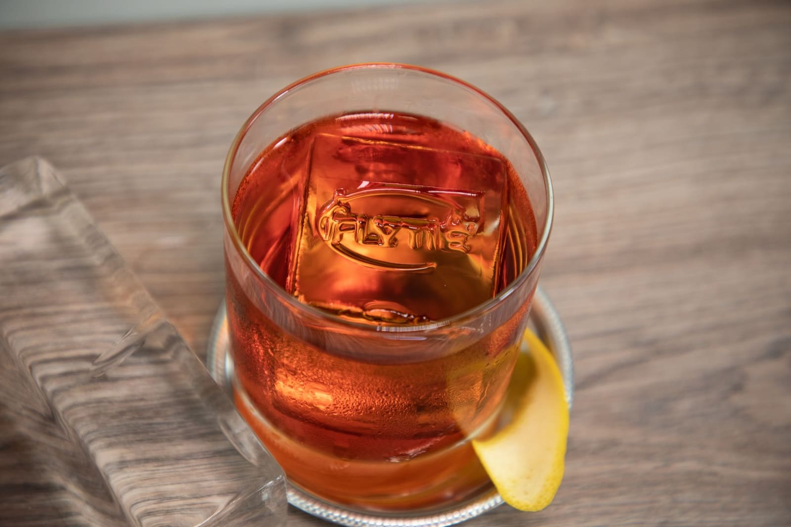 Glas whisky met grote ijsblokken en citroenschijfje op houten tafel.