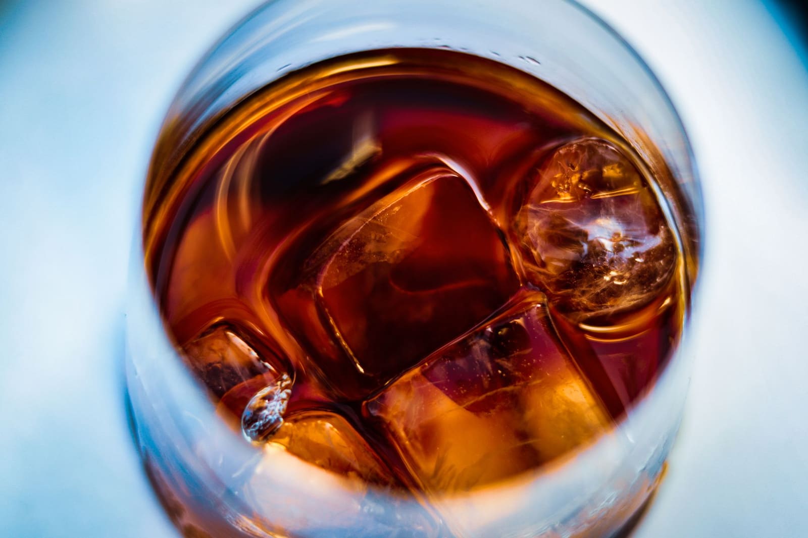 Glas bourbon whiskey met een ijsblokje op een houten bar