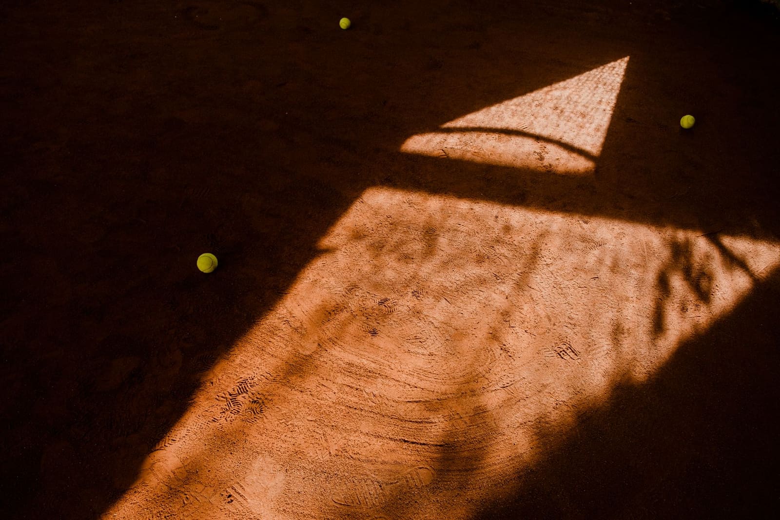 Gele tennisballen liggen op een rood gravel tennisveld