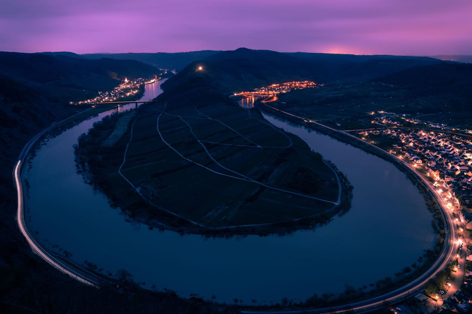 Luchtfoto bij schemering van een rivierbocht met glooiende wijngaardheuvels en verlichte dorpjes.