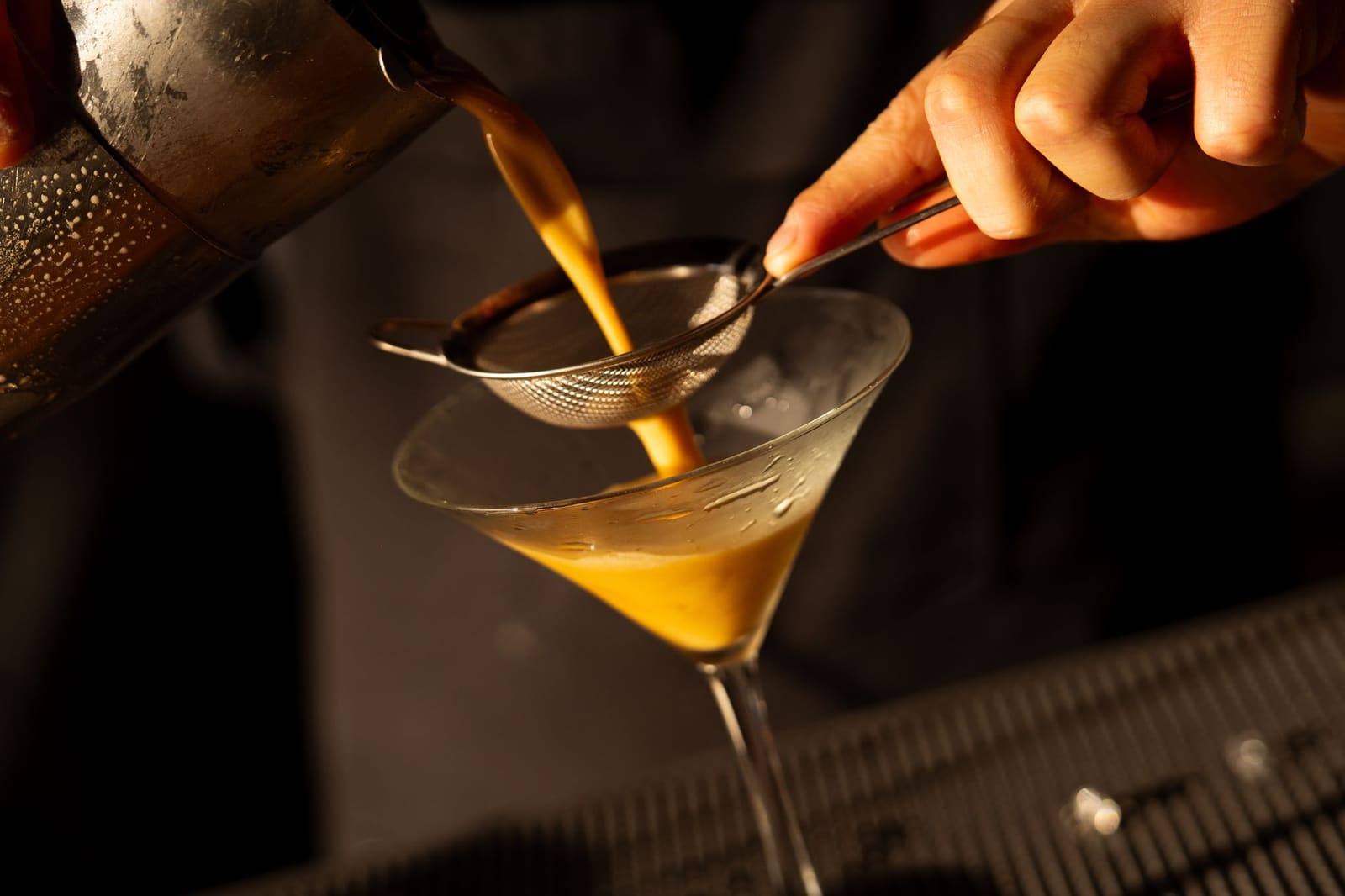 Bartender zeeft een cocktail uit de shaker in een martiniglas